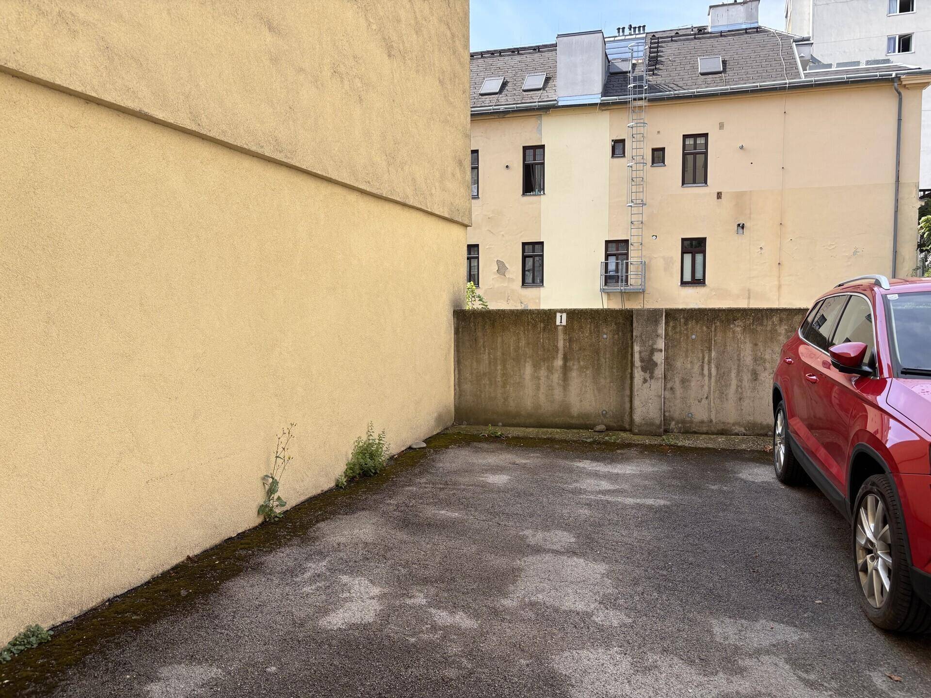 Außenparkplatz neben einem Gebäude mit gelber Fassade, bietet Stellfläche für ein Fahrzeug.