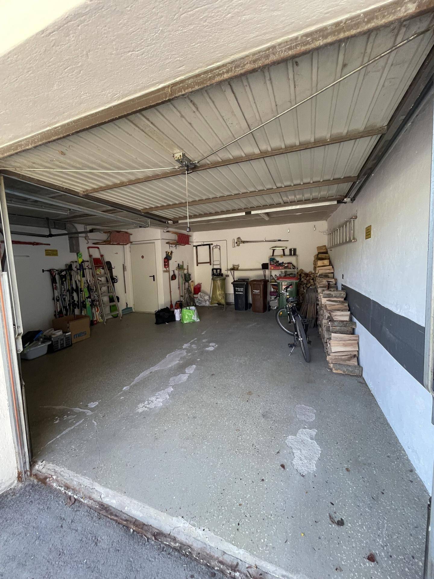 Geräumige Garage mit Betonboden, Stauraum und Holzstapel.