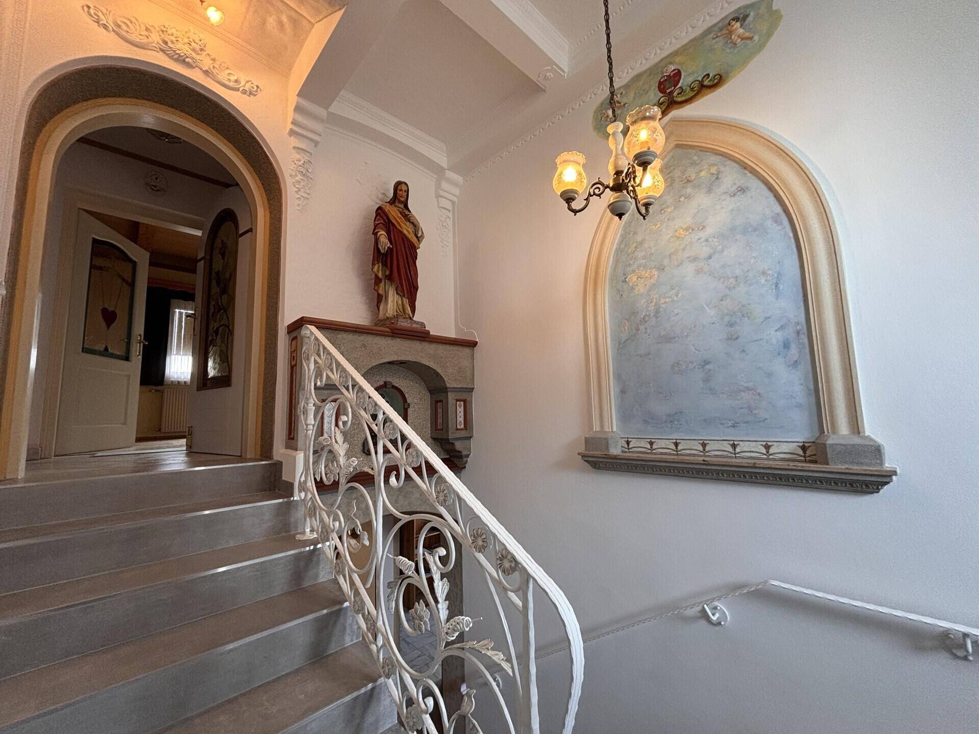 Repräsentatives Treppenhaus mit kunstvollem Geländer, Stuckverzierungen und einer Statue.