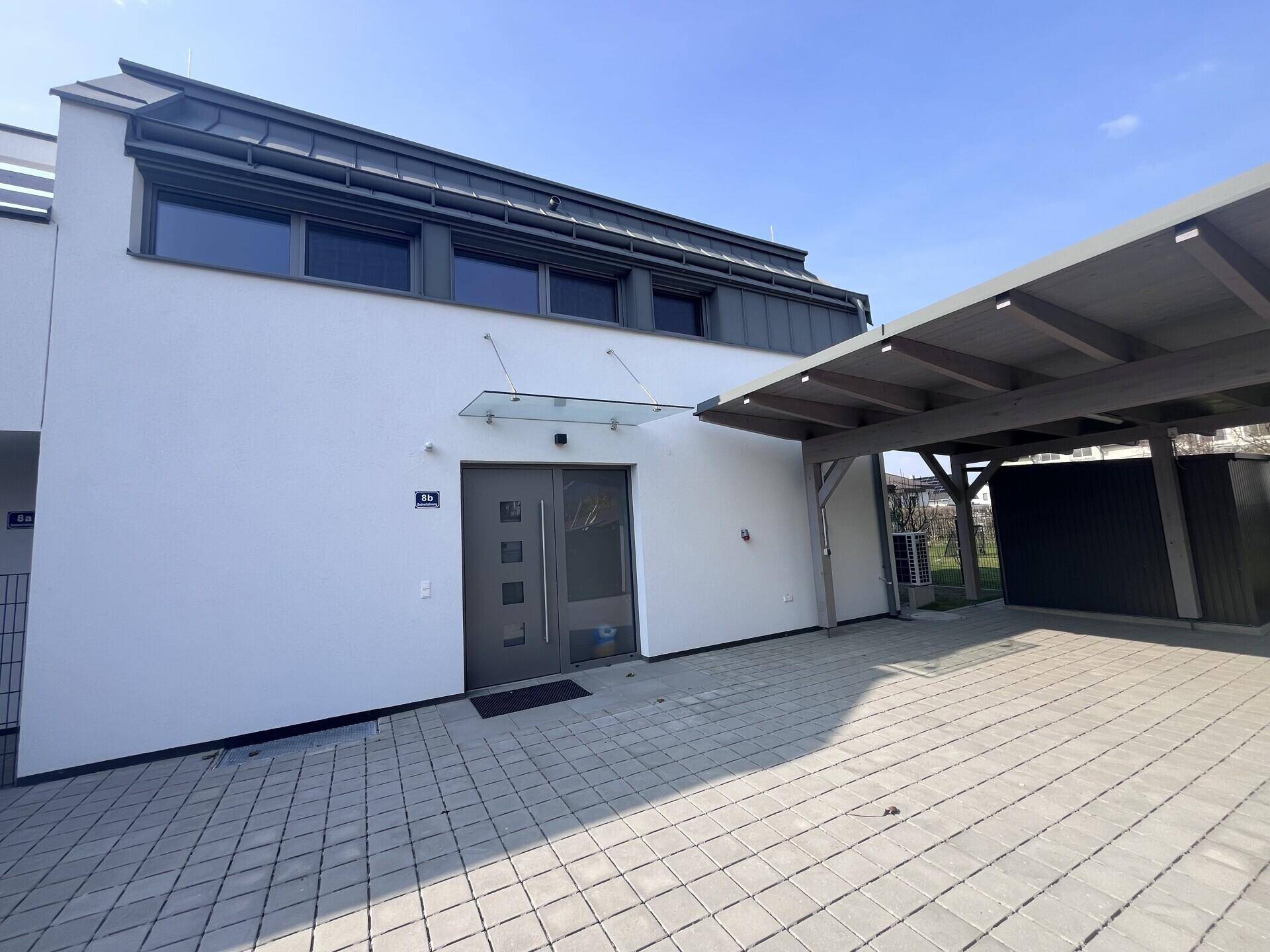Eingangsbereich der modernen Doppelhaushälfte mit Carport und gepflasterter Zufahrt.
