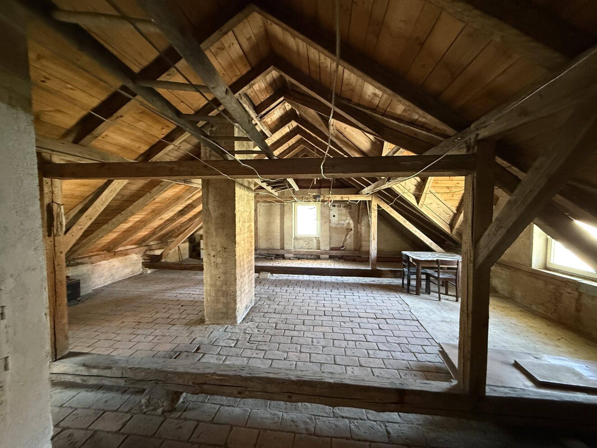 Weitläufiger Dachboden mit sichtbarer Holzkonstruktion und mehreren Fenstern, bietet Ausbaupotenzial.