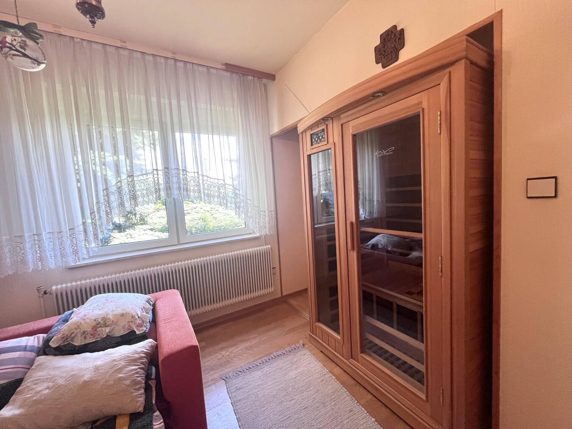Raum mit einer Infrarotsauna-Kabine, großem Fenster und hellem Holzfußboden.