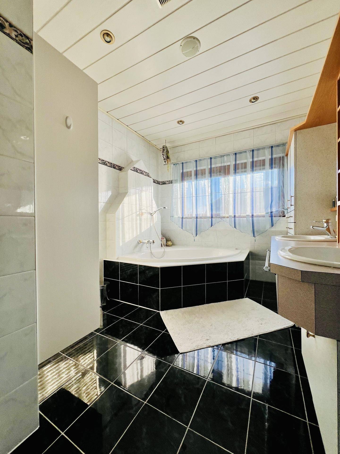 Badezimmer mit schwarzem Fliesenboden, Eckbadewanne und weißen Wandfliesen.