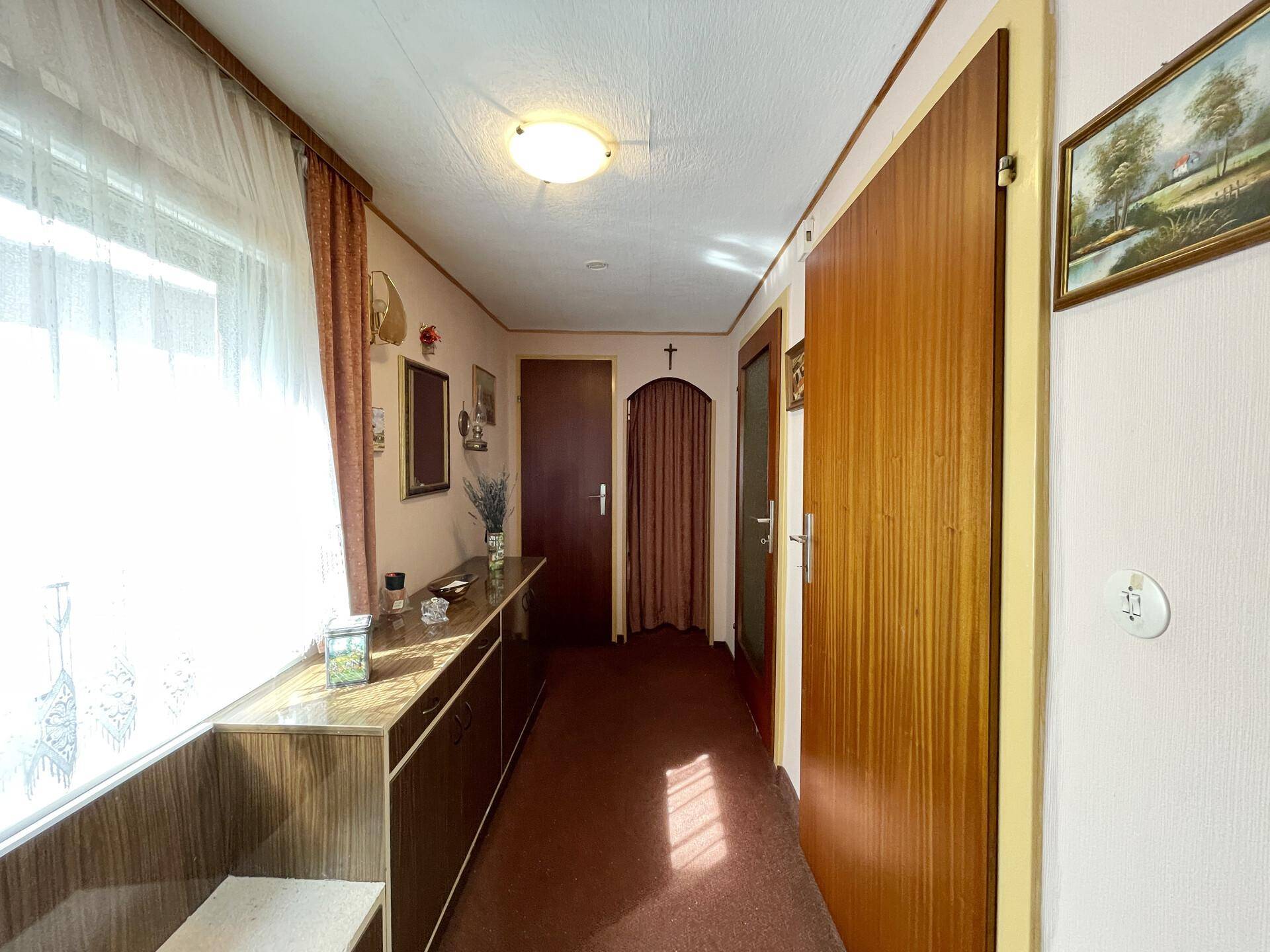 Heller Flur mit Fenster, Teppichboden und Holzvertäfelung an den Türen.