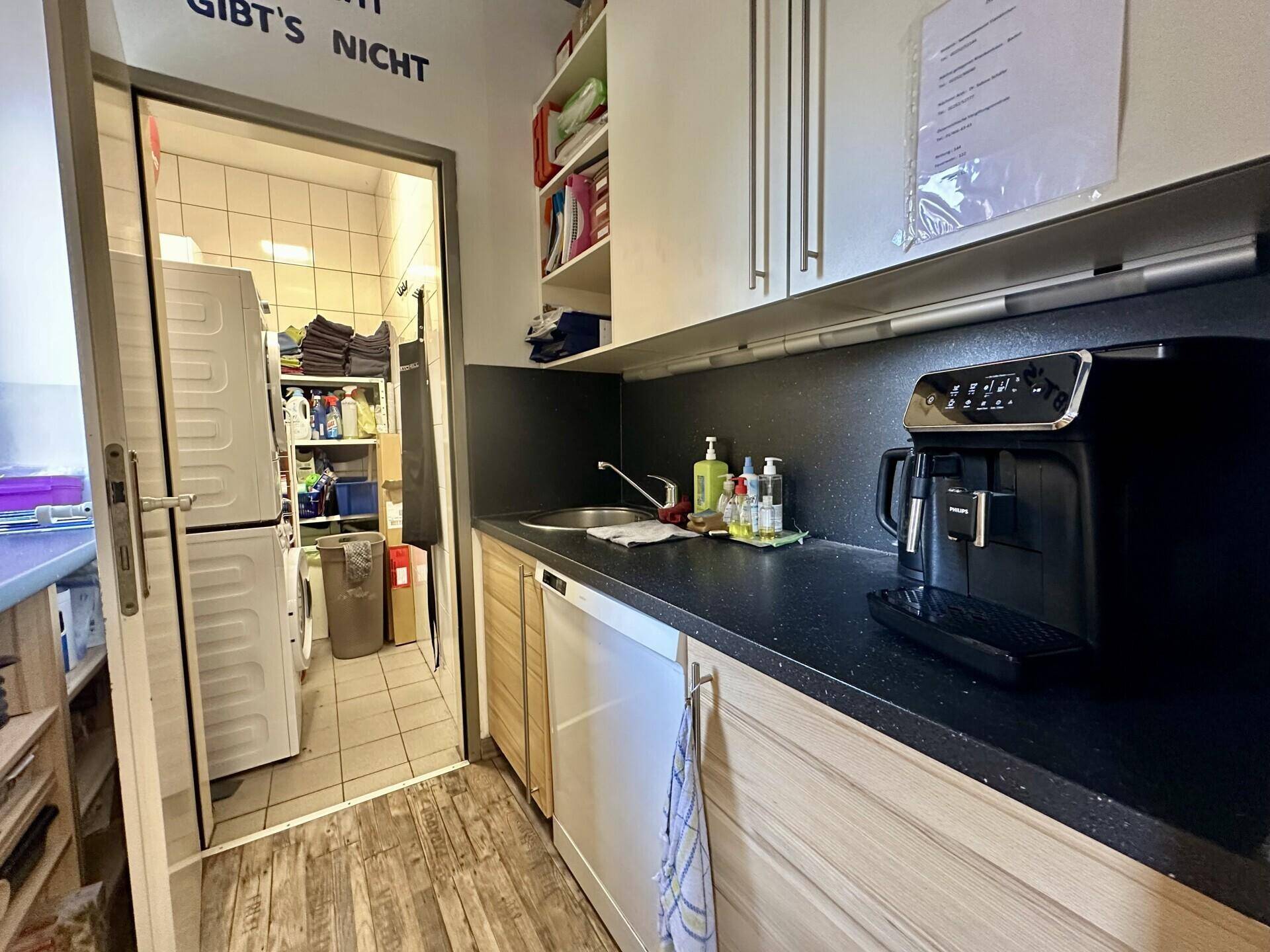 Praktische Teeküche mit Spüle, Kaffeemaschine und Stauraum, angrenzend an einen Waschraum.