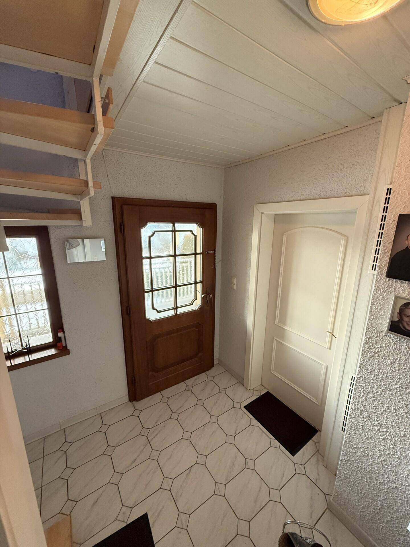 Eingangsbereich mit Holztür und Fliesenboden, angrenzend an die Treppe.