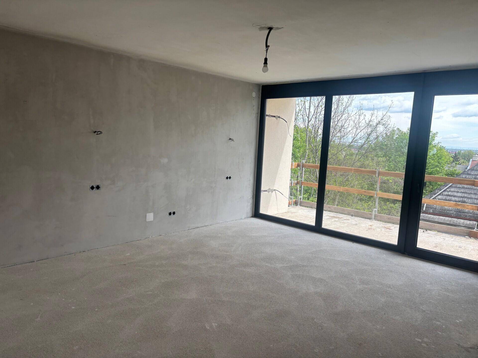 Heller, unfertiger Raum mit großen Fenstern und Zugang zu einem zukünftigen Balkon.