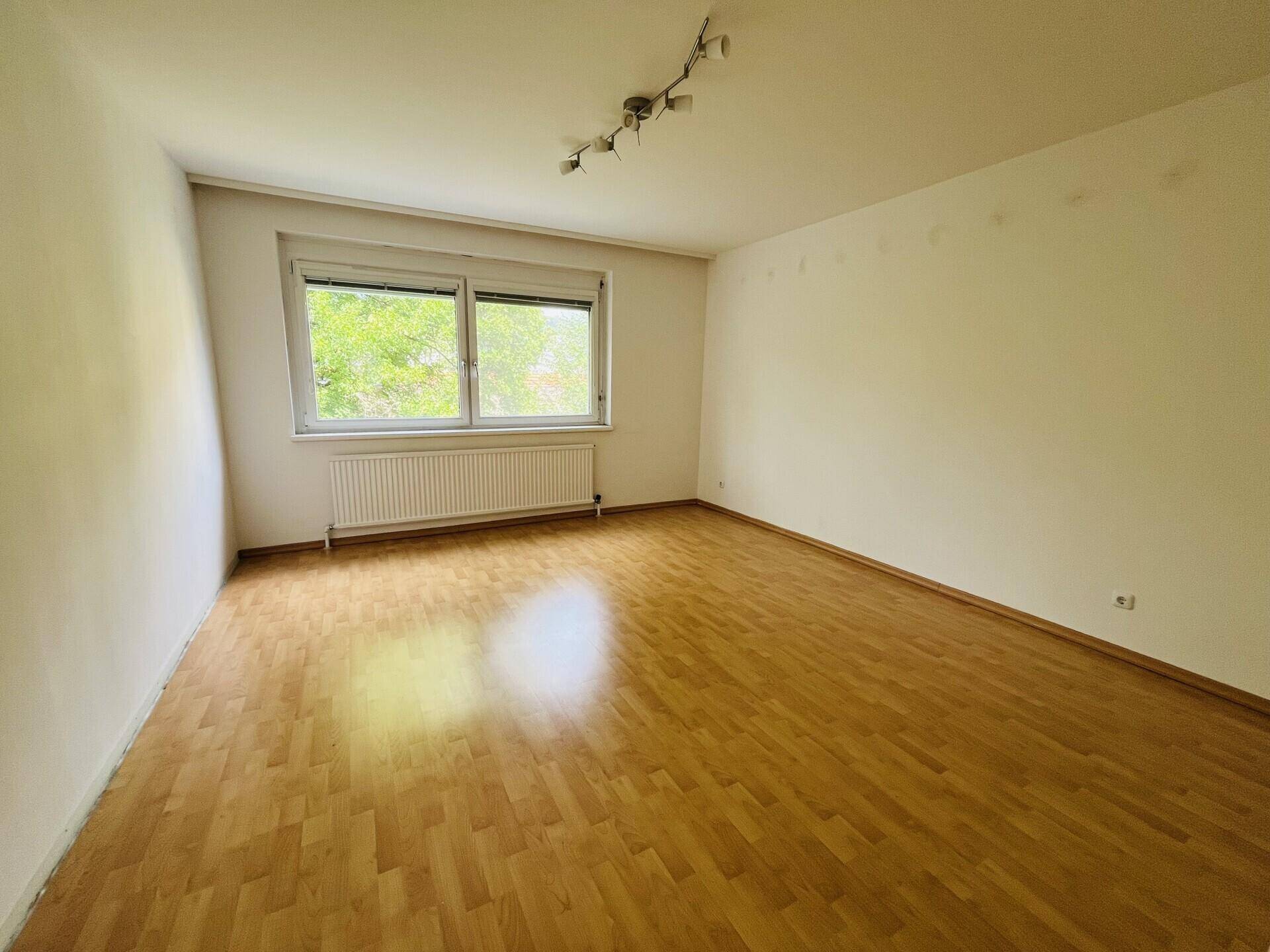 Helles Schlafzimmer mit Parkettboden und Fenster, das viel Tageslicht hereinlässt.
