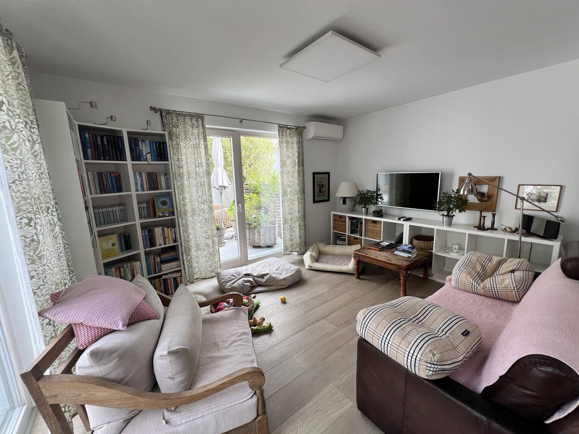 Helles Wohnzimmer mit Holzboden, Bücherregalen und Zugang zu einer Außenterrasse.