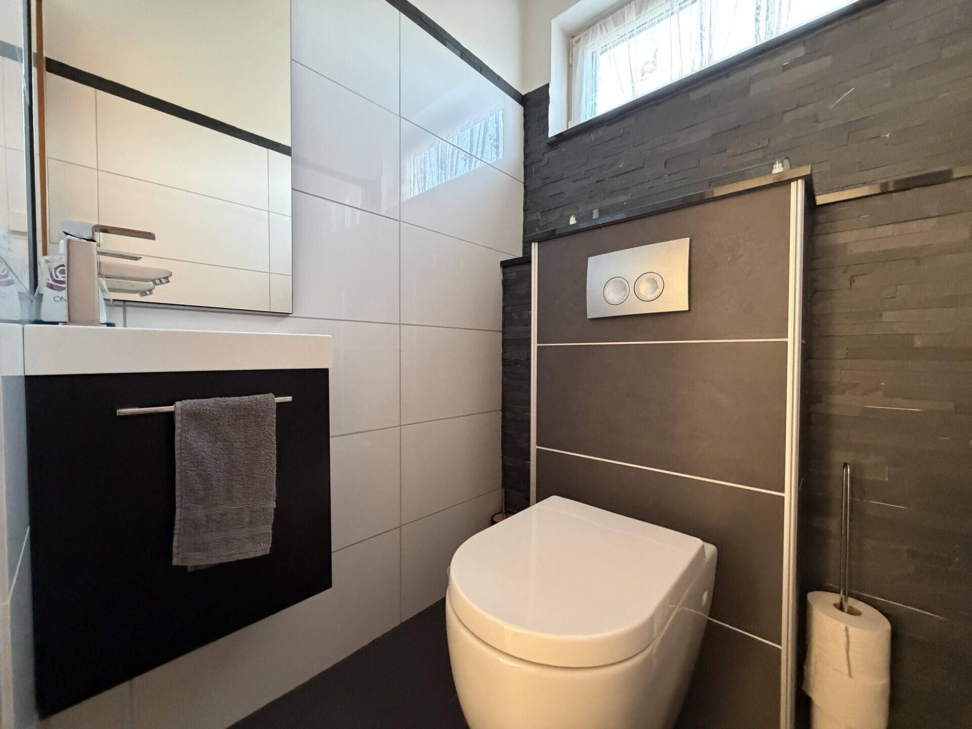 Modernes Gäste-WC mit dunklen und weißen Fliesen, wandhängendem WC und kleinem Waschbecken.