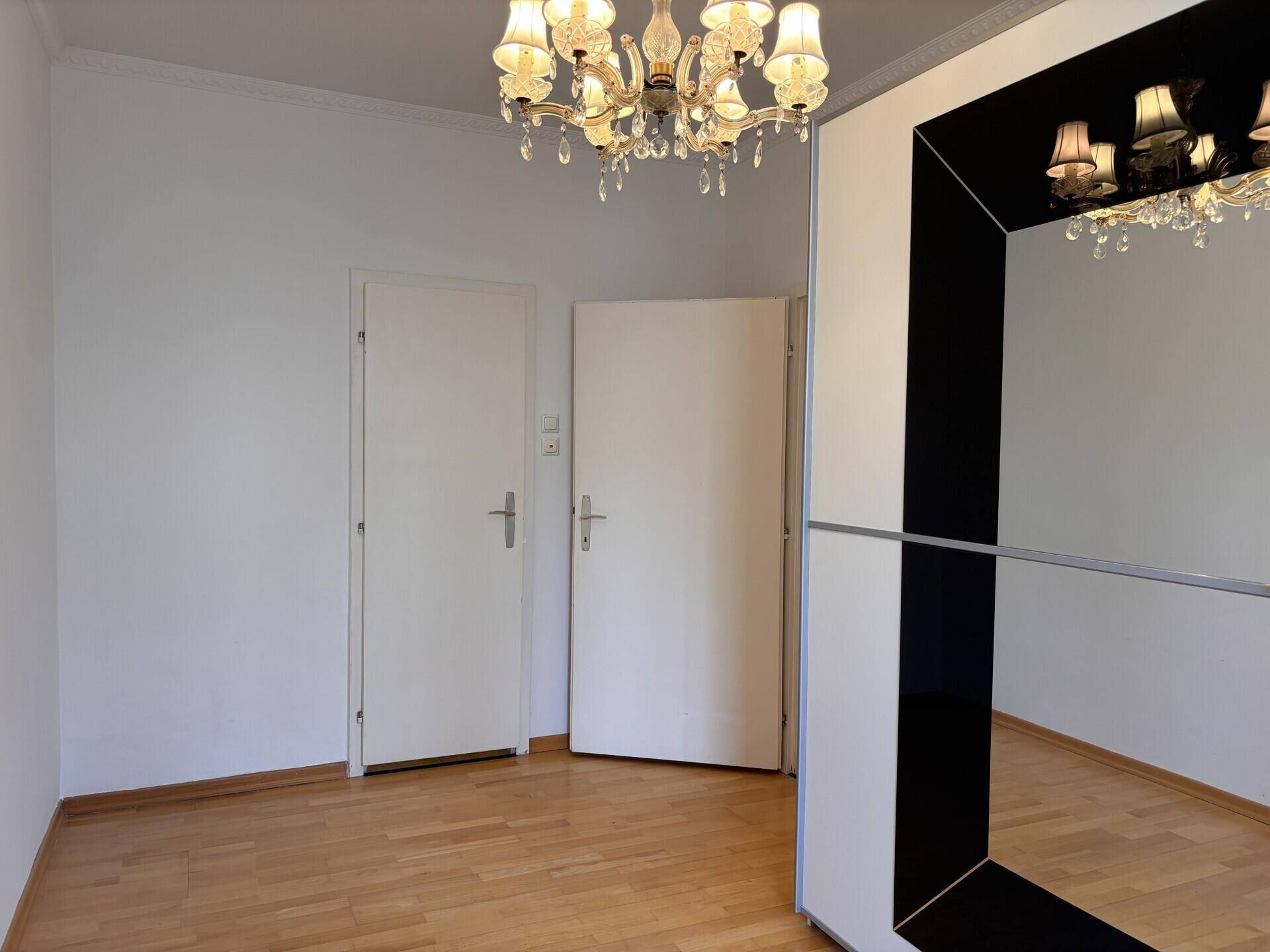 Schlafzimmer mit Holzboden, Spiegelschrank und zwei Türen, die Zugang zu weiteren Bereichen bieten.