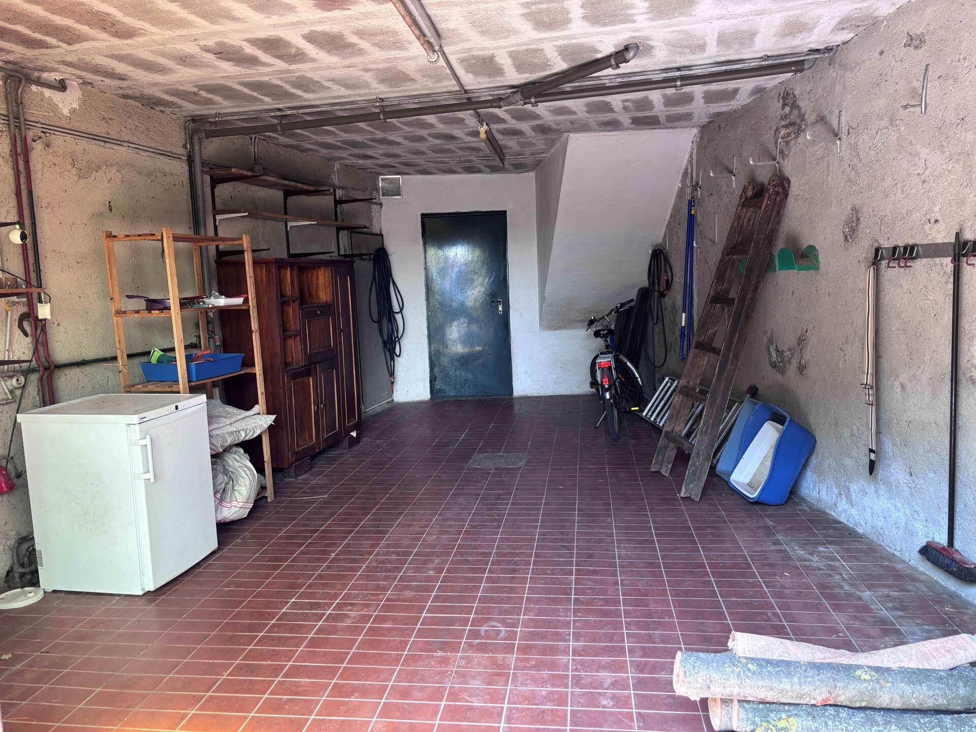 Geräumige Garage oder Abstellraum mit Fliesenboden, Lagerregalen und sichtbaren Leitungen.