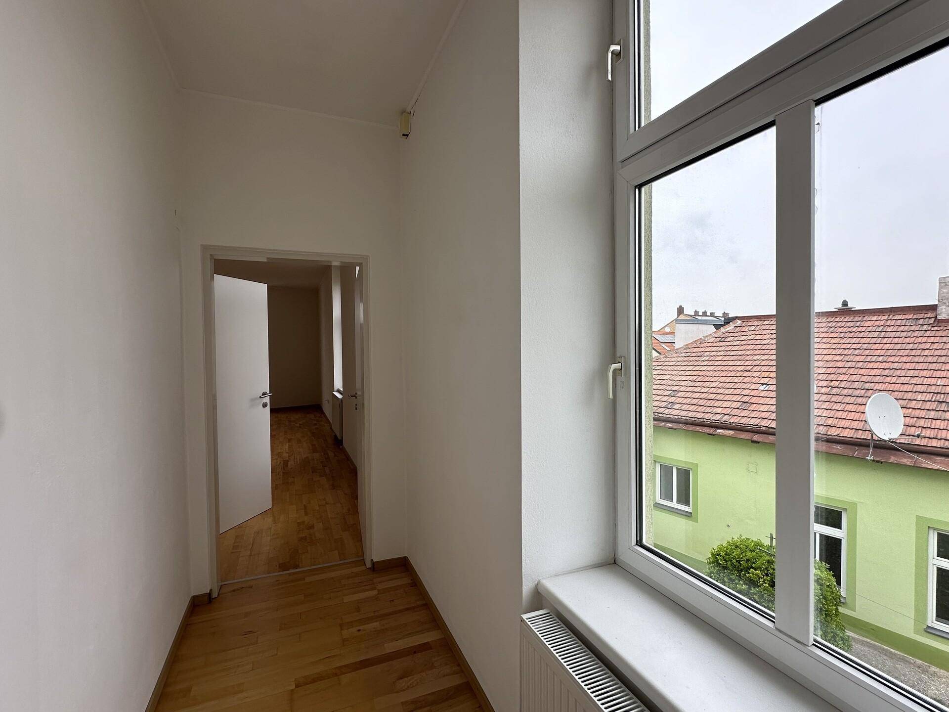 Heller Flur mit Parkettboden und Blick auf die Nachbarhäuser durch das große Fenster.