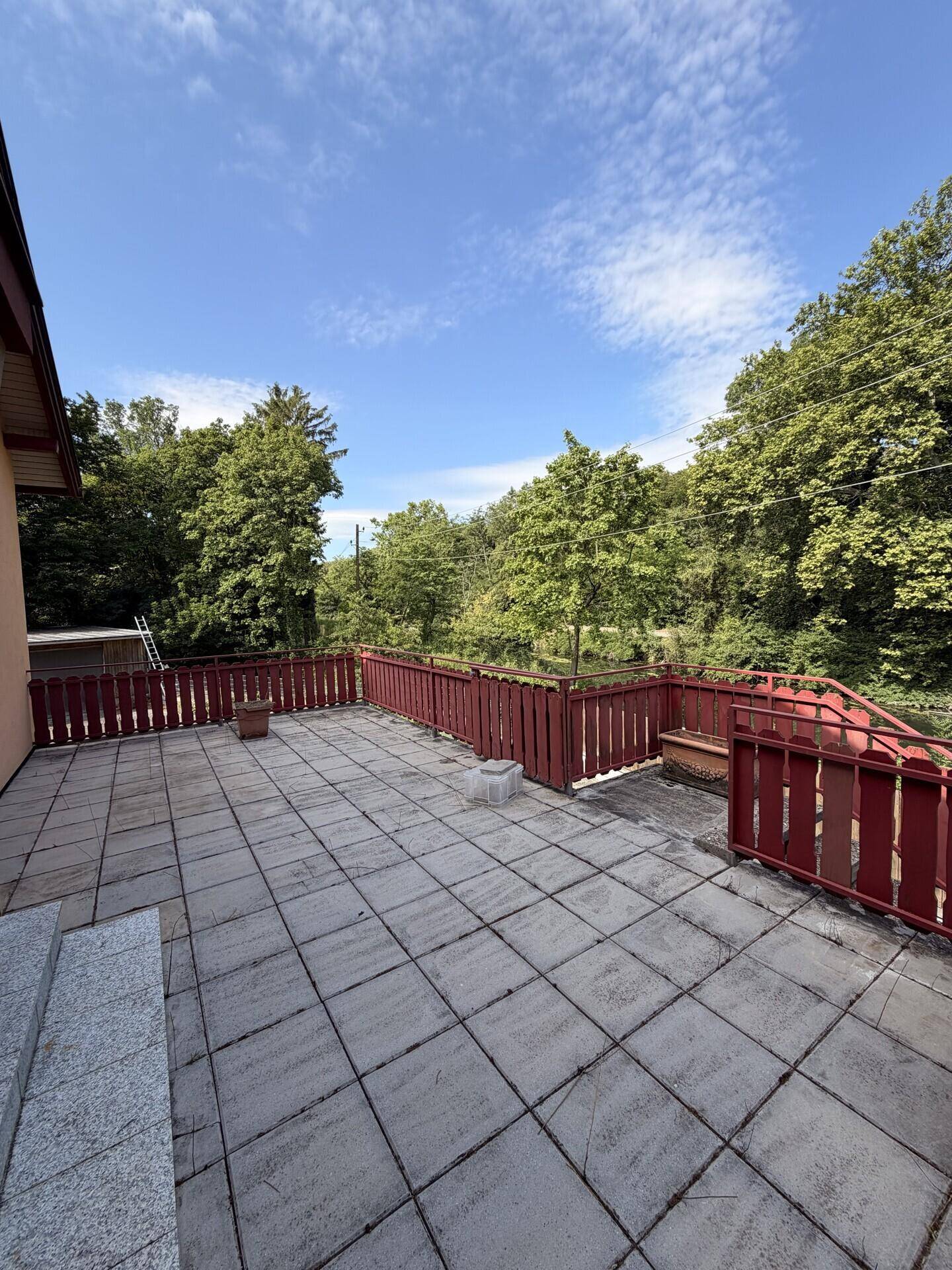 Große geflieste Terrasse mit rotem Geländer und weitem Blick in die grüne Umgebung.