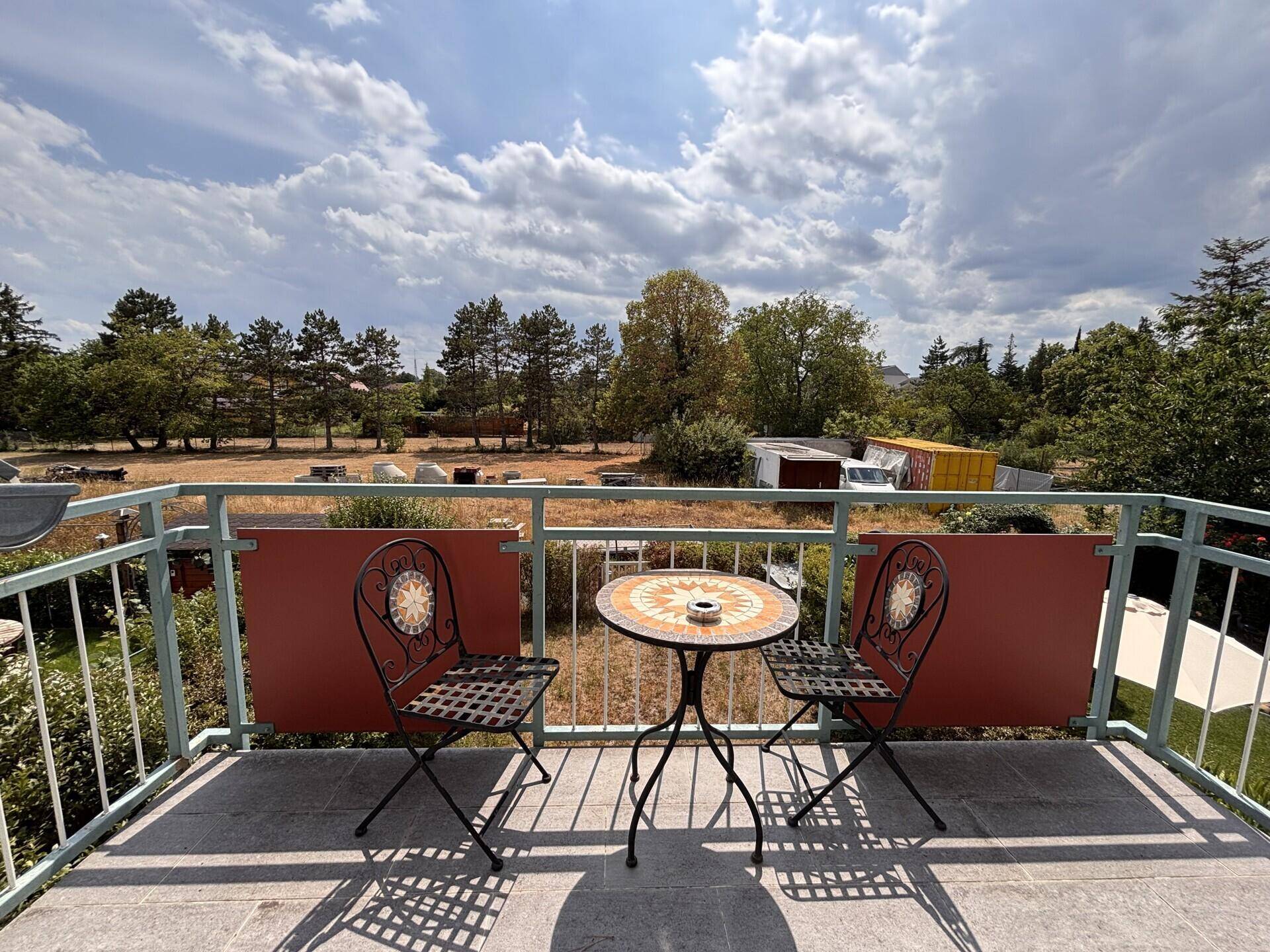 Balkon mit Mosaiktisch und Stühlen, bietet einen weiten Blick ins Grüne.
