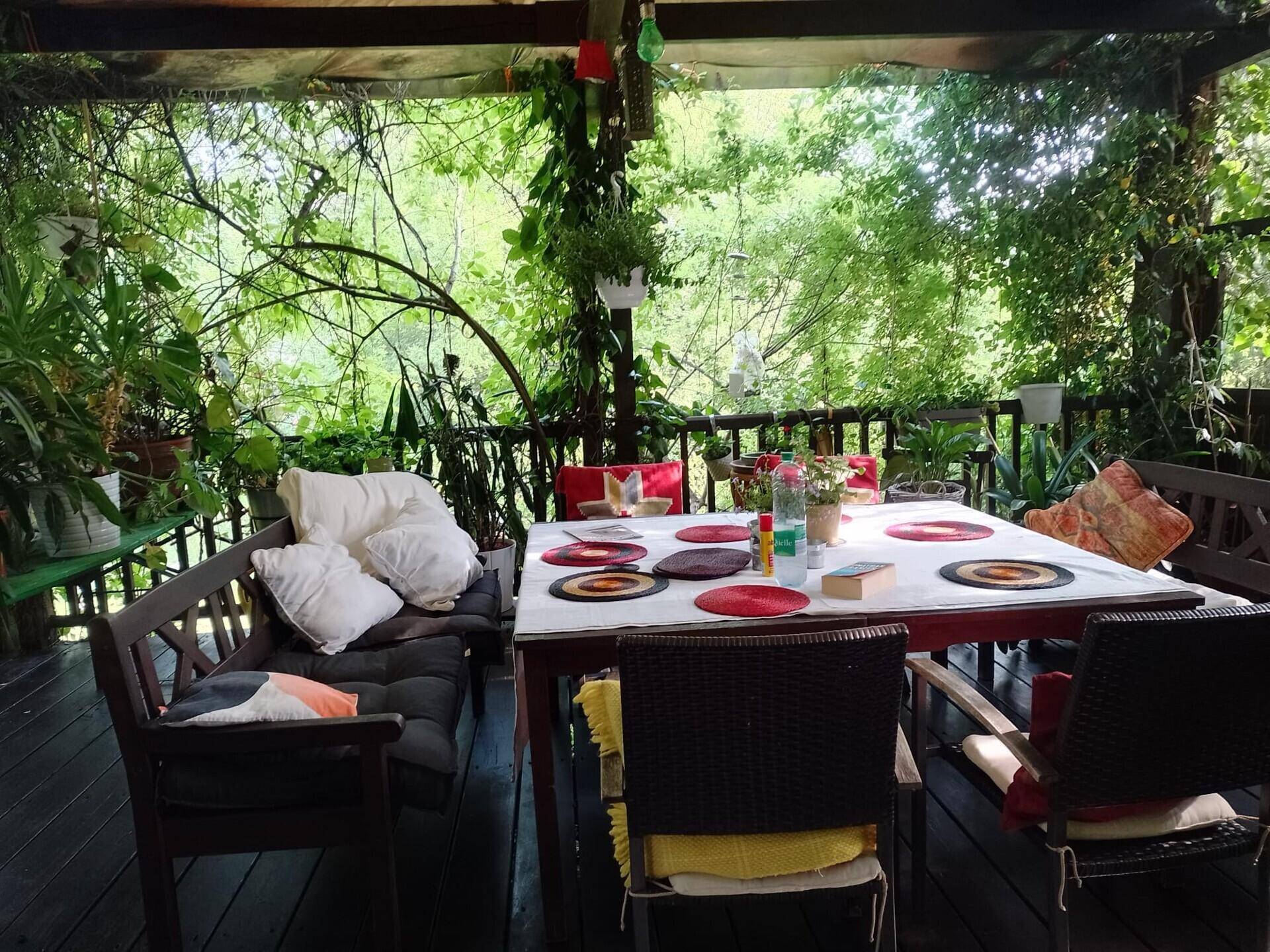 Überdachte Terrasse mit Esstisch und bequemen Sitzgelegenheiten, umgeben von Pflanzen.
