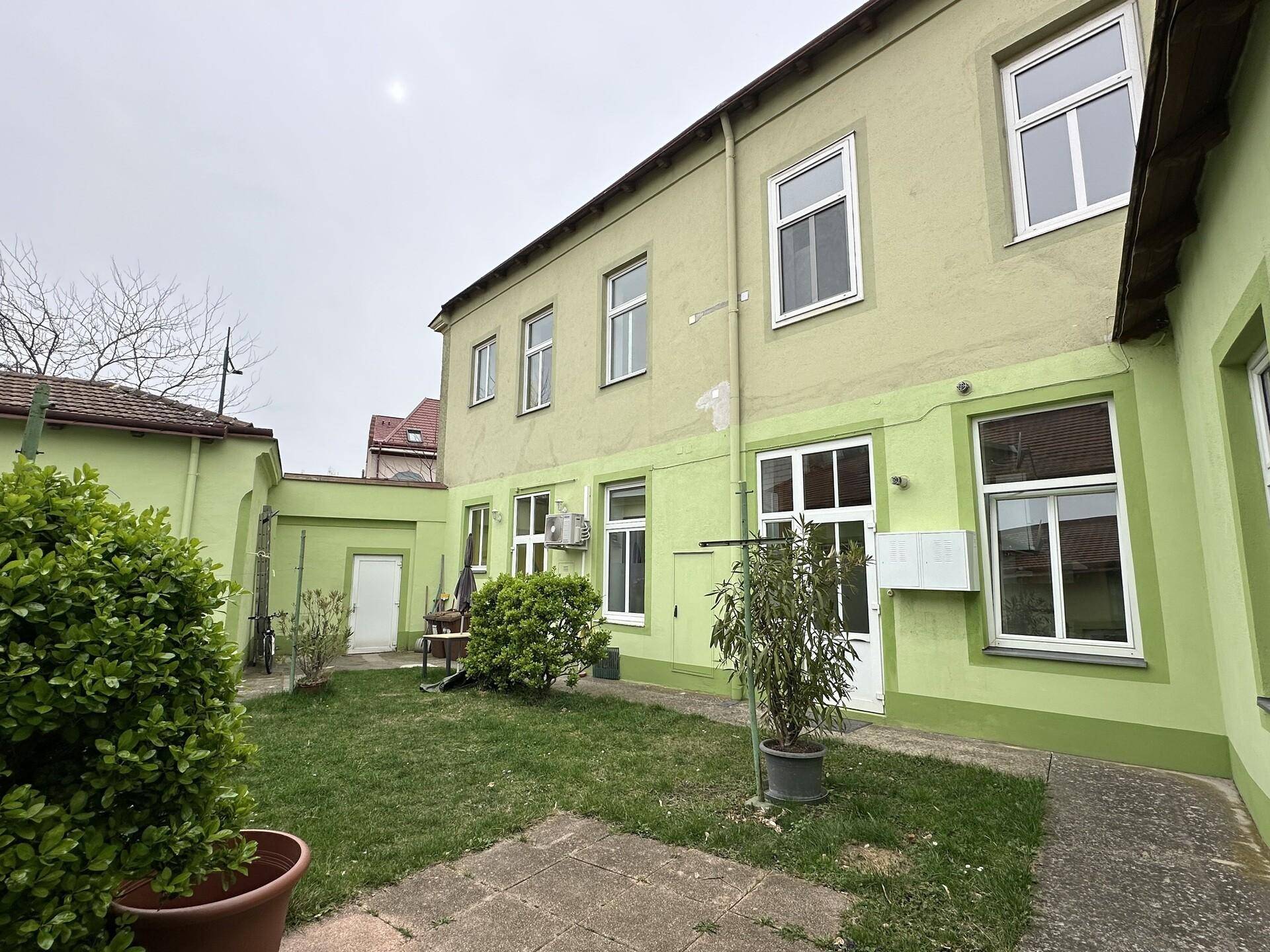 Kleiner Hinterhof mit Rasen, umgeben von den Gebäudeteilen und einem gepflasterten Weg.