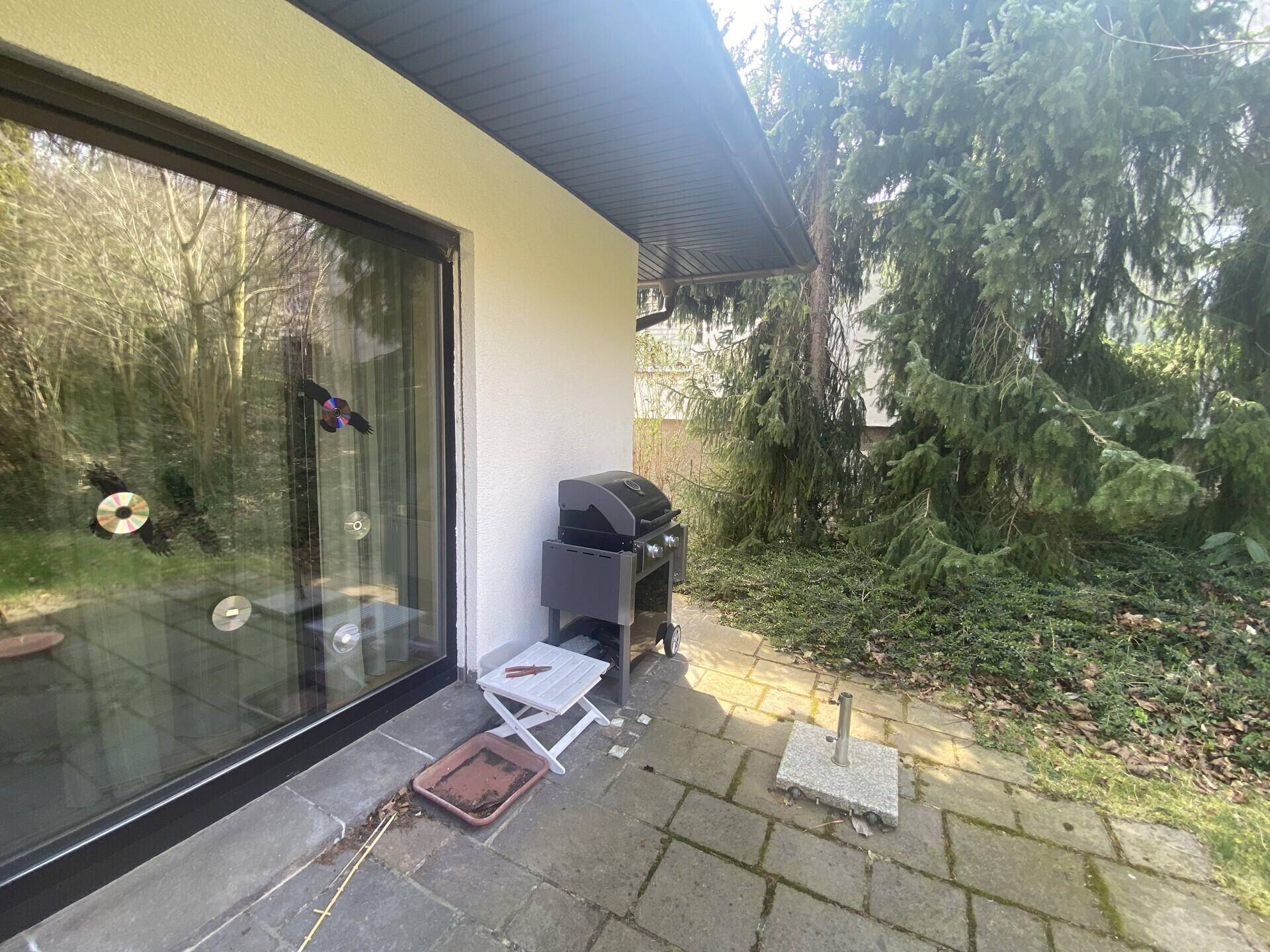 Gepflasterter Bereich neben dem Haus mit Grill und Zugang zum Garten.