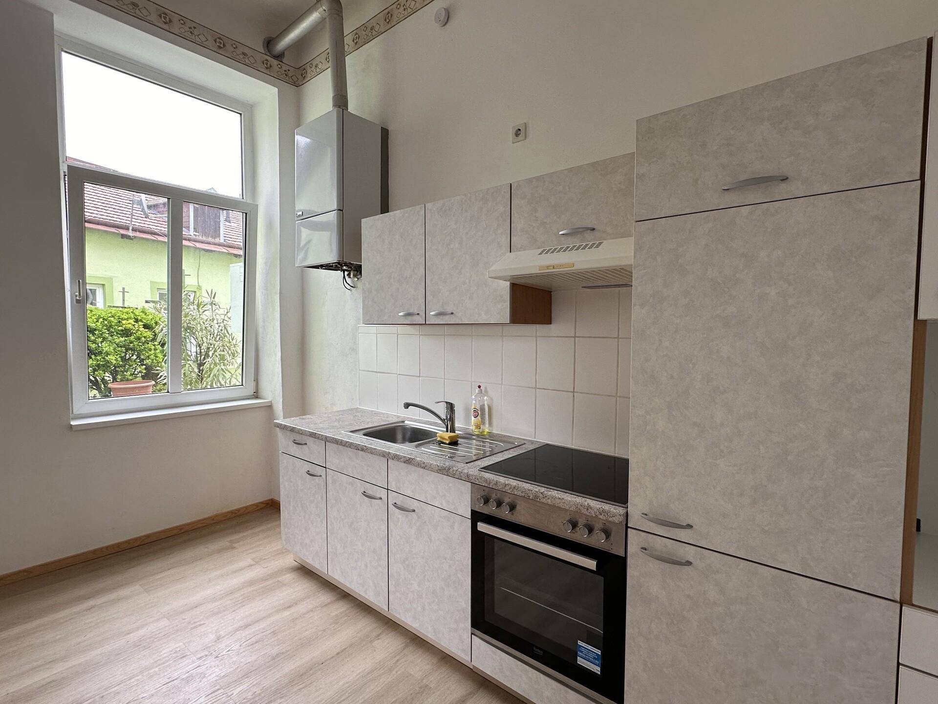Funktionale Küche mit Einbauschränken, Spüle und Kochfeld, mit Blick ins Grüne durch das Fenster.