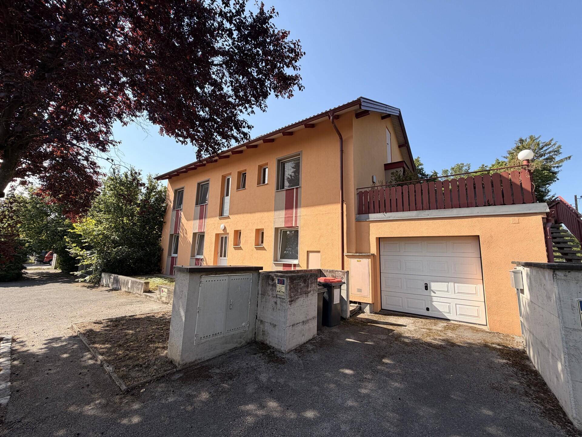 Gebäude mit orangefarbener Fassade, Garage und gepflasterter Einfahrt unter blauem Himmel.