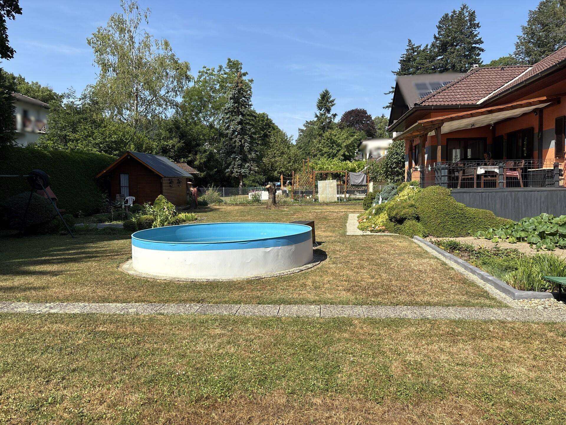 Großer Gartenbereich mit Rasenfläche, einem Aufstellpool und viel Grün.