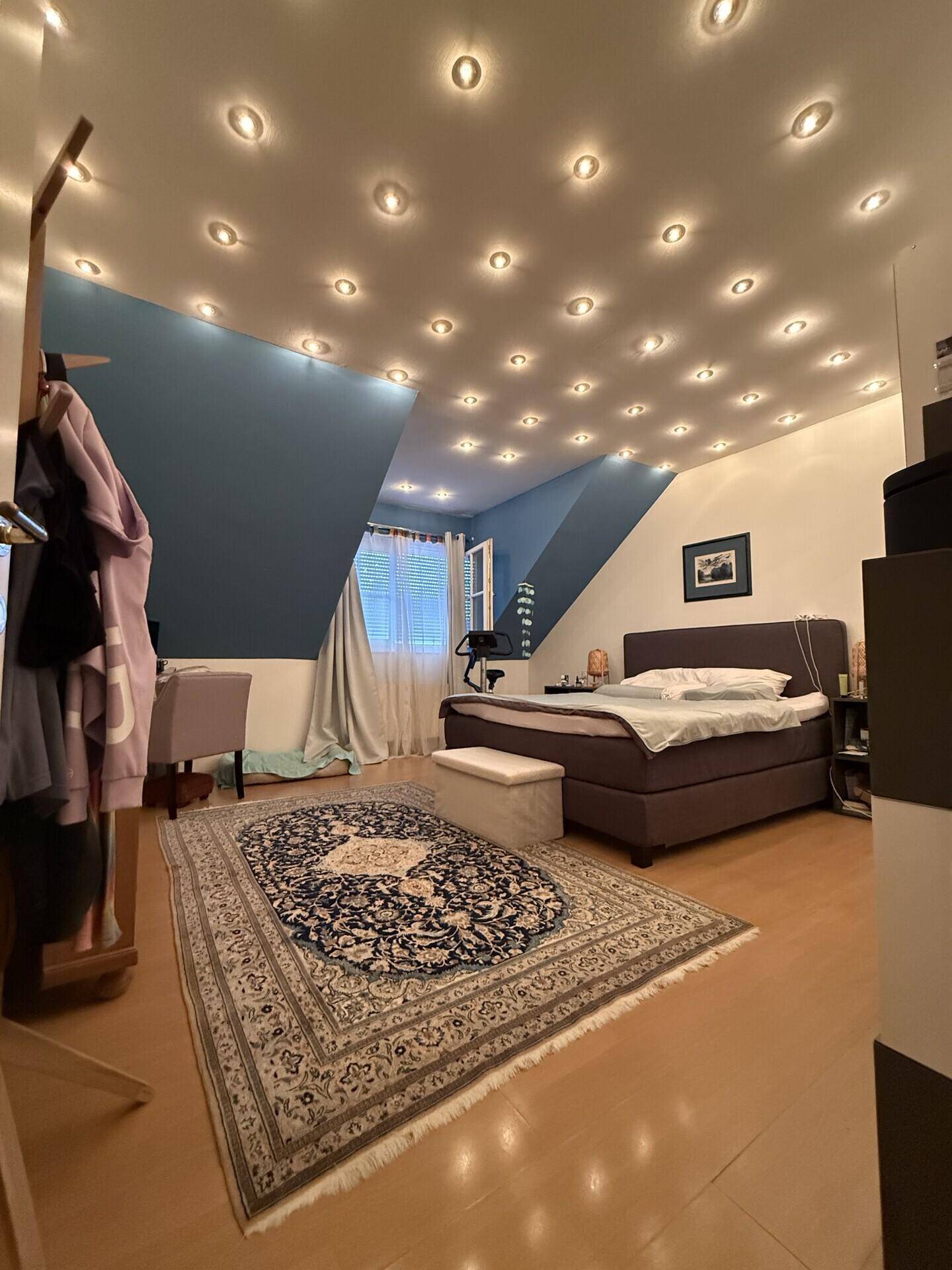 Schlafzimmer im Dachgeschoss mit blauer Akzentwand, Einbaustrahlern und Teppich.