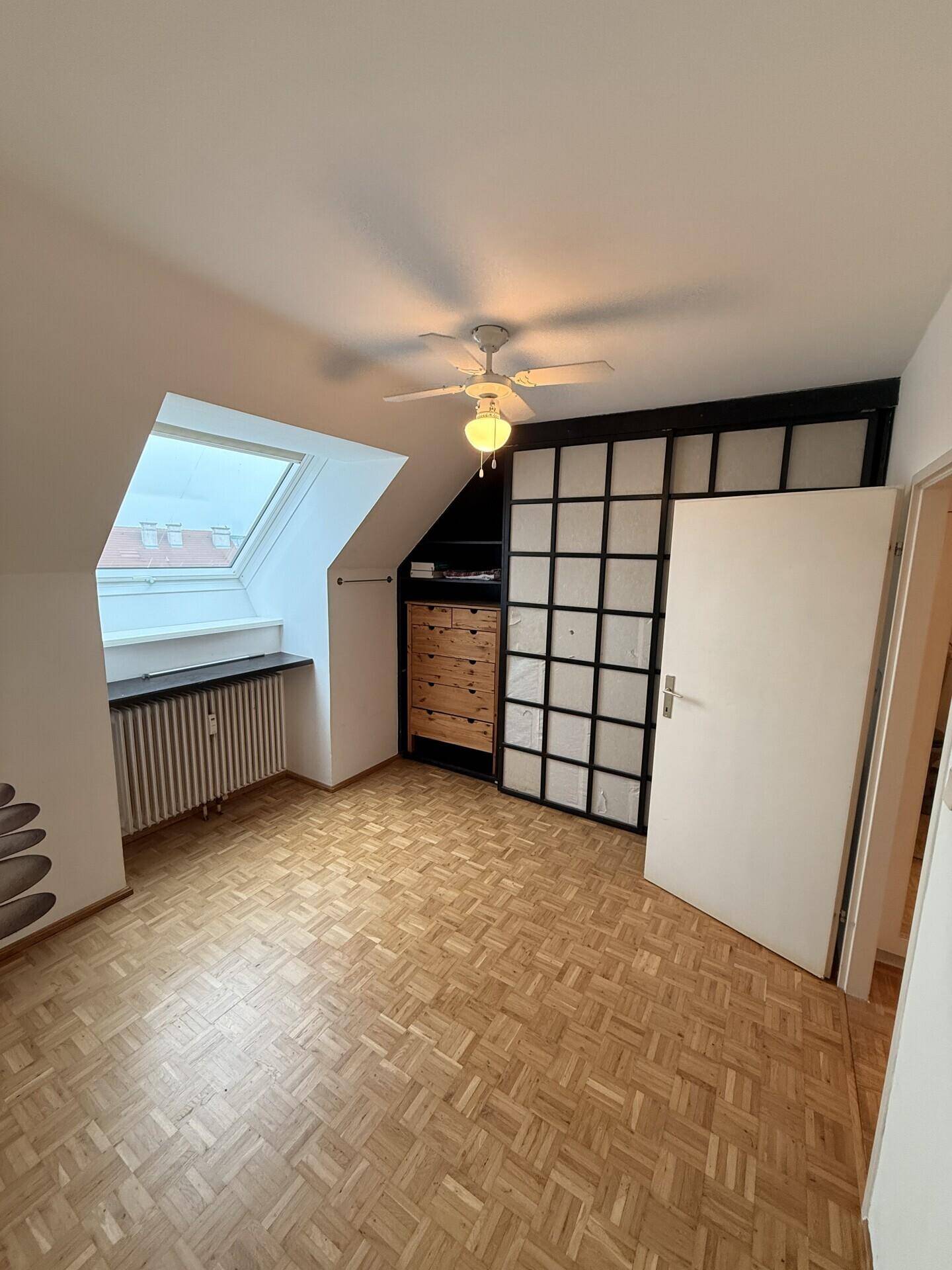 Helles Schlafzimmer mit Dachfenster, Parkettboden und integriertem Schrankbereich.