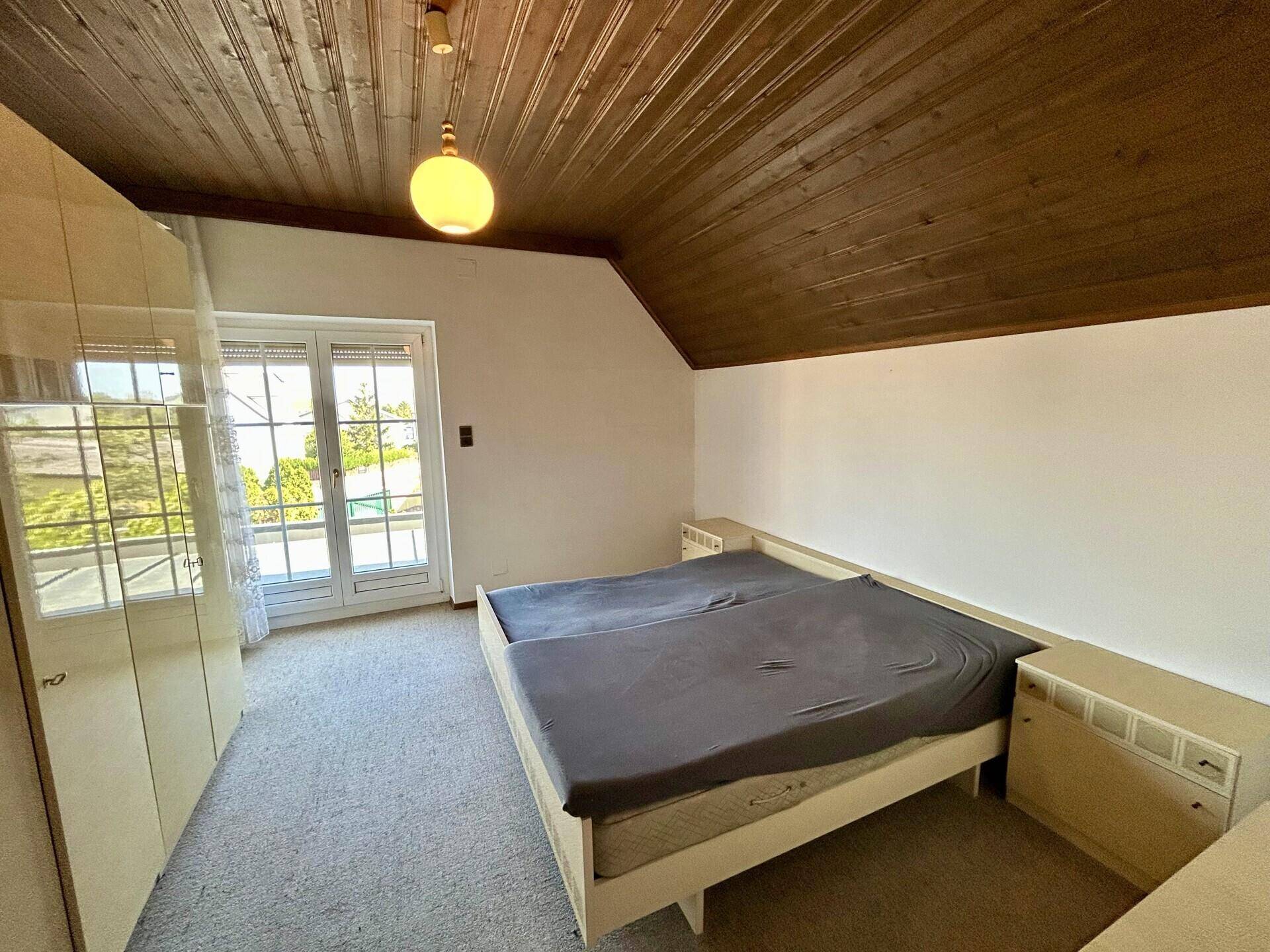 Helles Schlafzimmer im Dachgeschoss mit Holzdecke und Zugang zum Balkon.