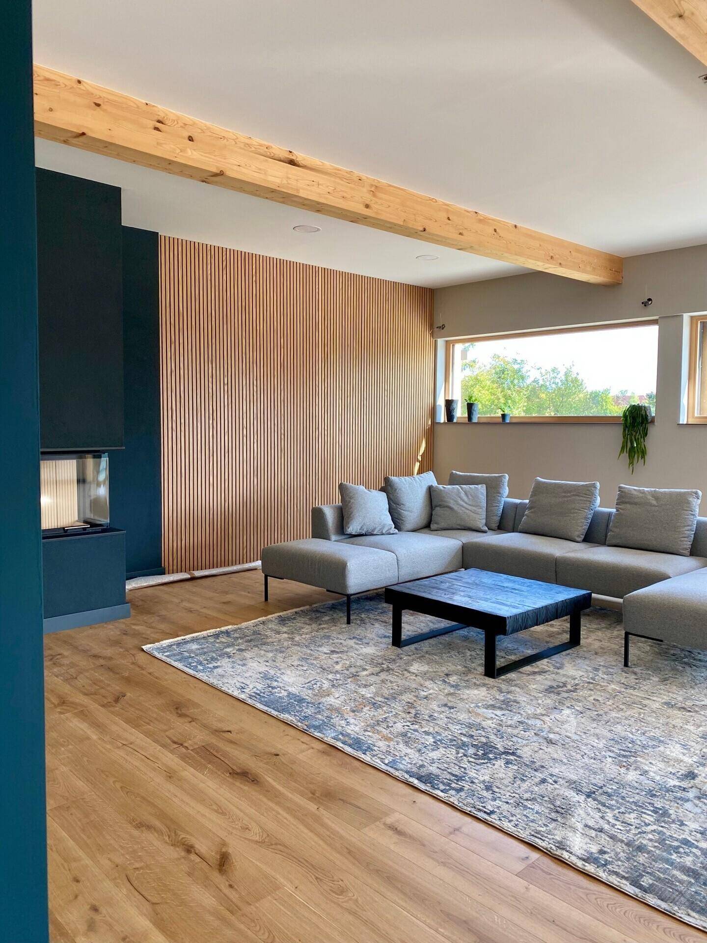 Helles Wohnzimmer mit großen Fenstern, Holzbalken und einem gemütlichen Kaminbereich.
