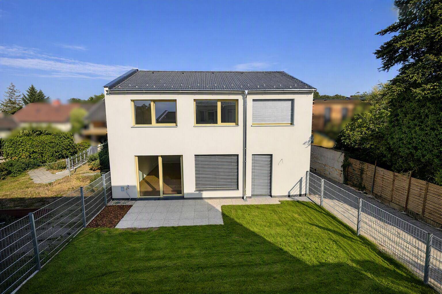 Rückansicht des modernen Hauses mit Garten, Terrasse und umlaufendem Zaun.
