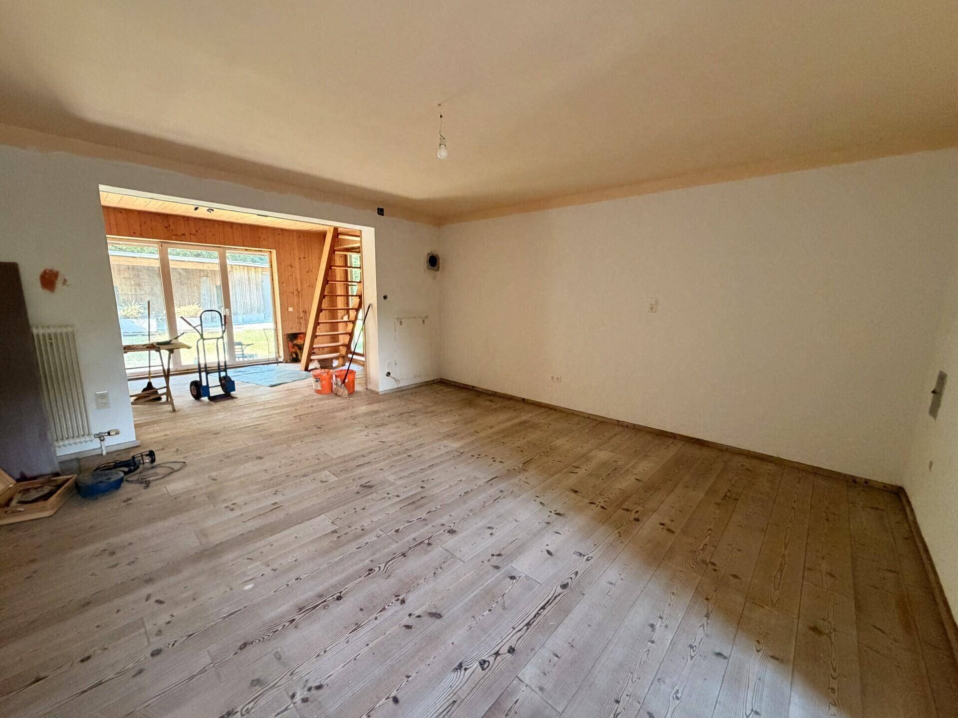 Geräumiges Wohnzimmer mit Holzdielenboden, weißen Wänden und Blick auf den Garten.