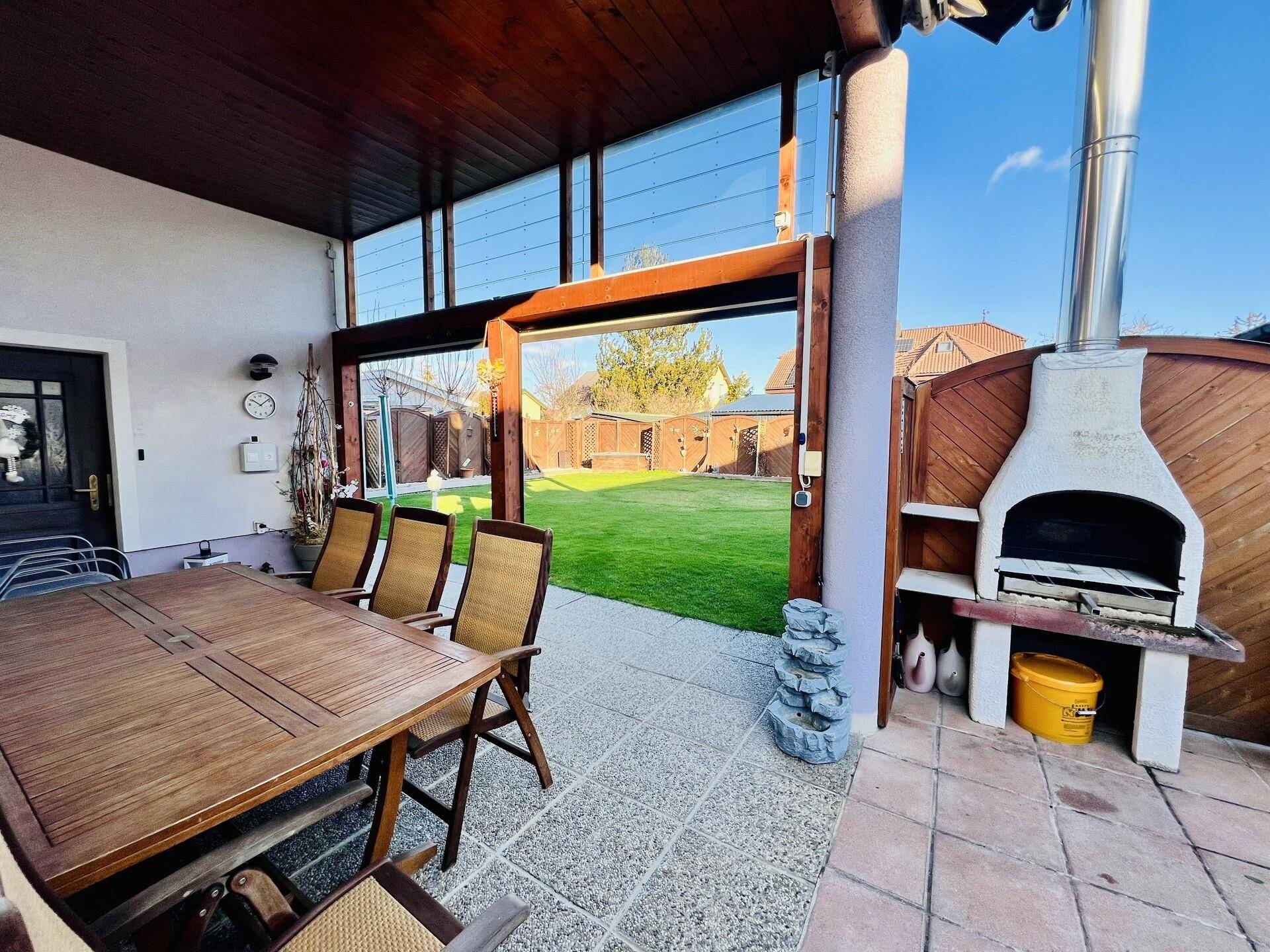 Überdachte Terrasse mit Esstisch, Stühlen und einem gemauerten Grillbereich mit Gartenblick.