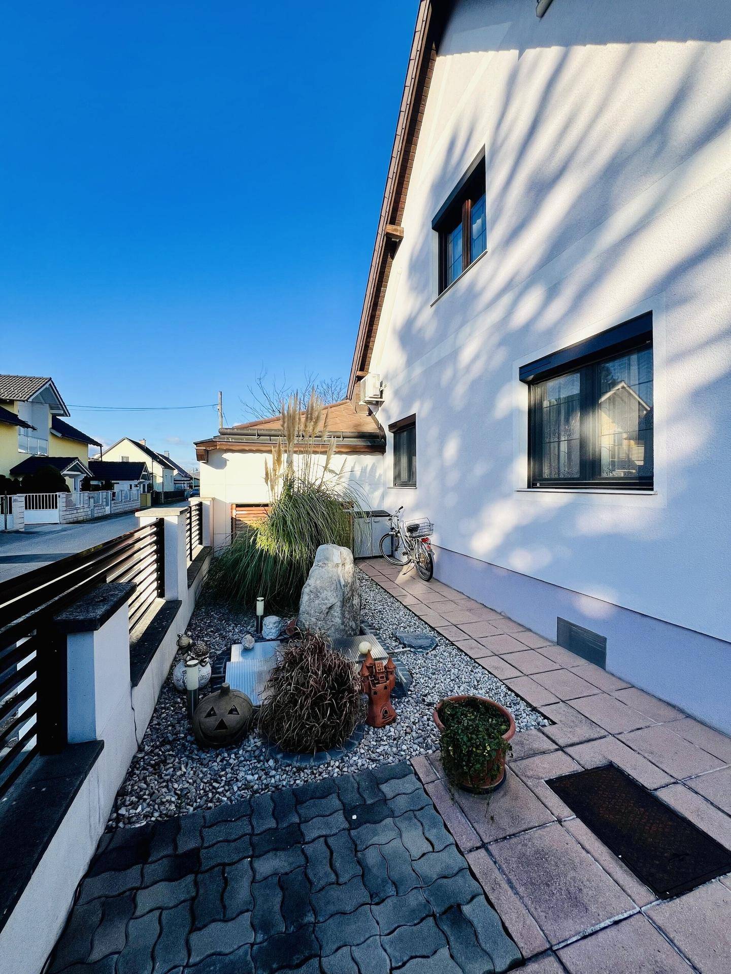 Seitlicher Zugang zum Haus mit Kiesbeet, dekorativen Steinen und einem gepflasterten Weg.