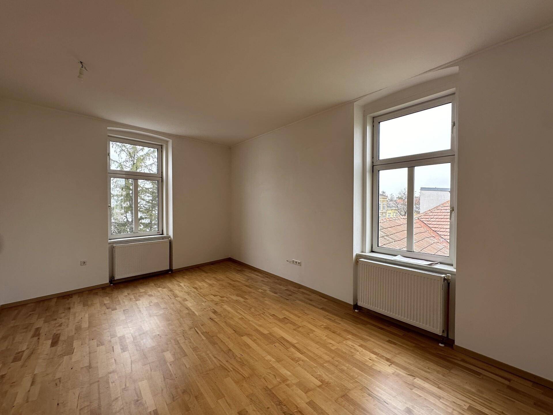 Helles Schlafzimmer mit Parkettboden und zwei Fenstern, bietet eine angenehme und ruhige Atmosphäre.