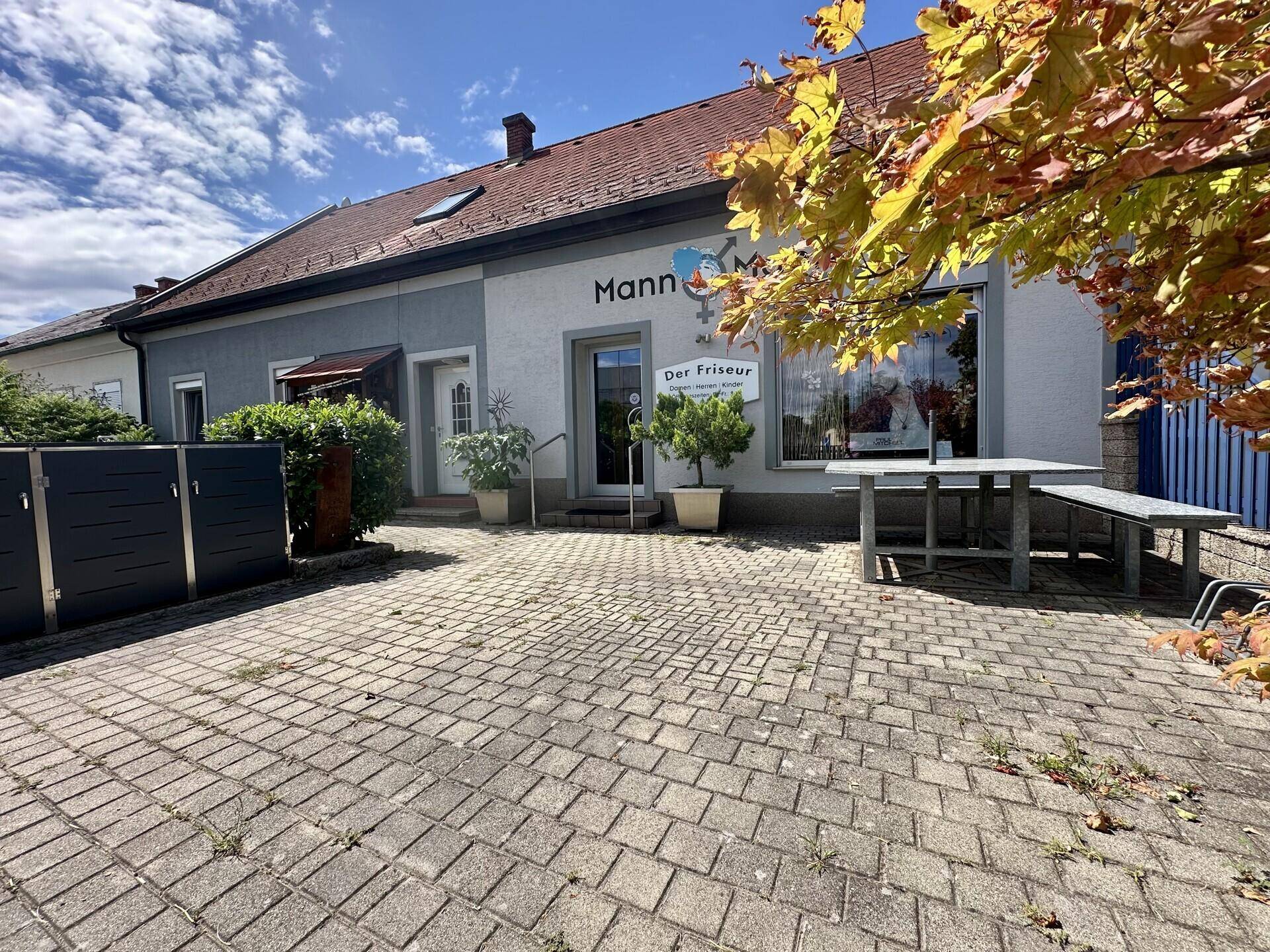 Eingangsbereich des Friseursalons "Mann & Mann" mit gepflastertem Vorplatz und Pflanzen.