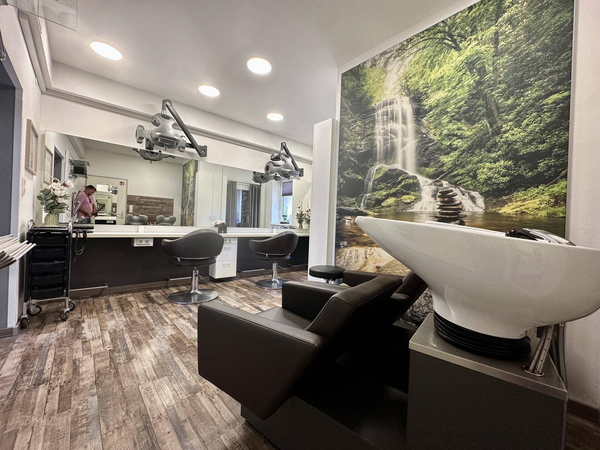 Waschbeckenbereich im Friseursalon mit großer Wandtapete und Styling-Stationen mit Spiegeln.
