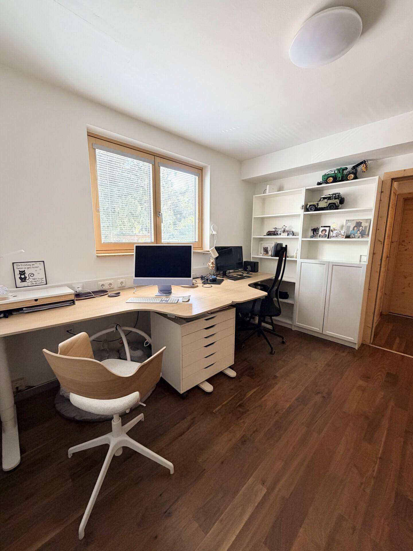 Helles Arbeitszimmer mit großem Schreibtisch, Regalen und Holzboden.