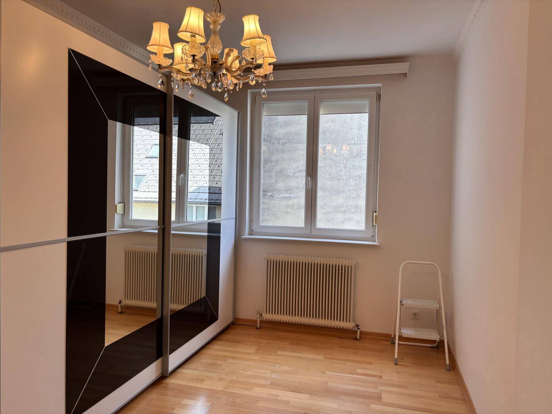 Helles Schlafzimmer mit Holzboden, Spiegelschrank und Fenster, das den Raum erhellt.