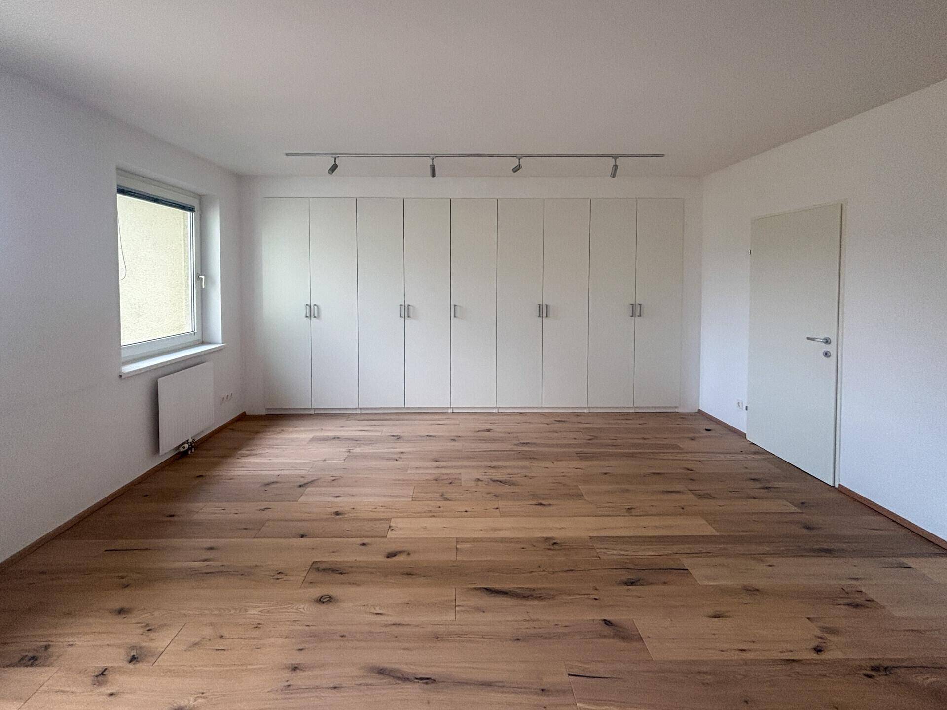 Helles Schlafzimmer mit Holzboden und einer langen Reihe von Einbauschränken.