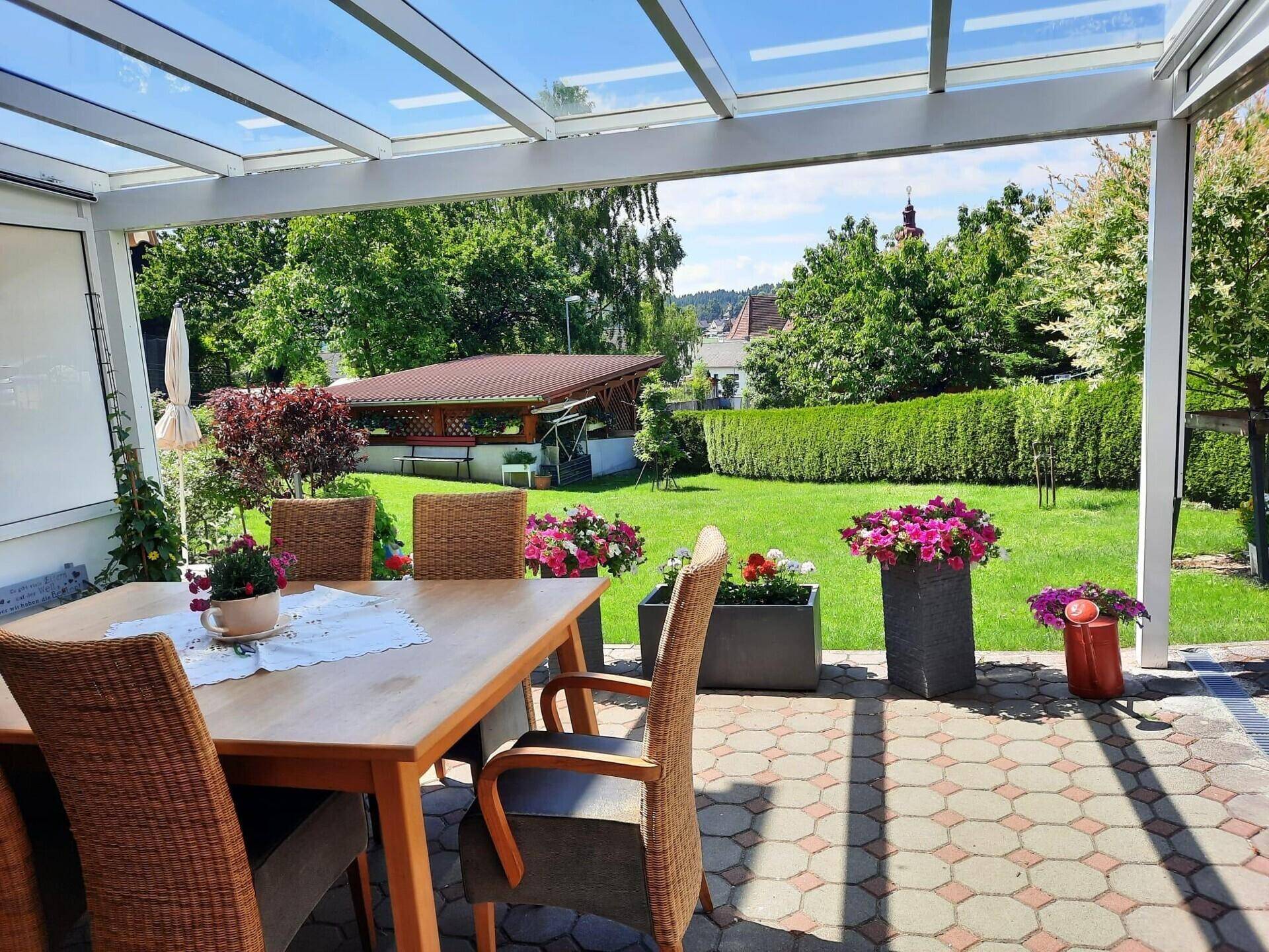 Blick von der überdachten Terrasse über den gepflegten Garten auf die umliegende Landschaft.