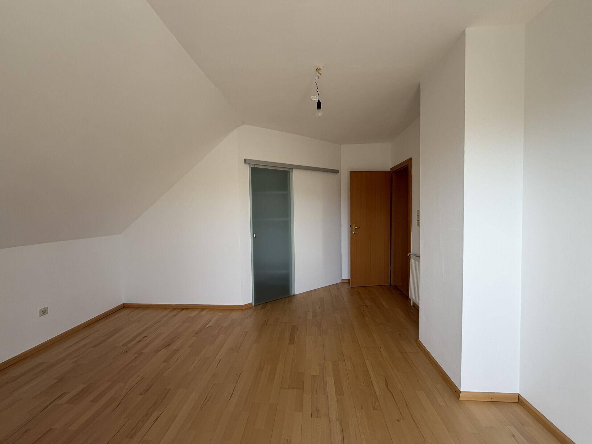 Geräumiges Schlafzimmer im Dachgeschoss mit Parkettboden, Dachschräge und Schiebetür.