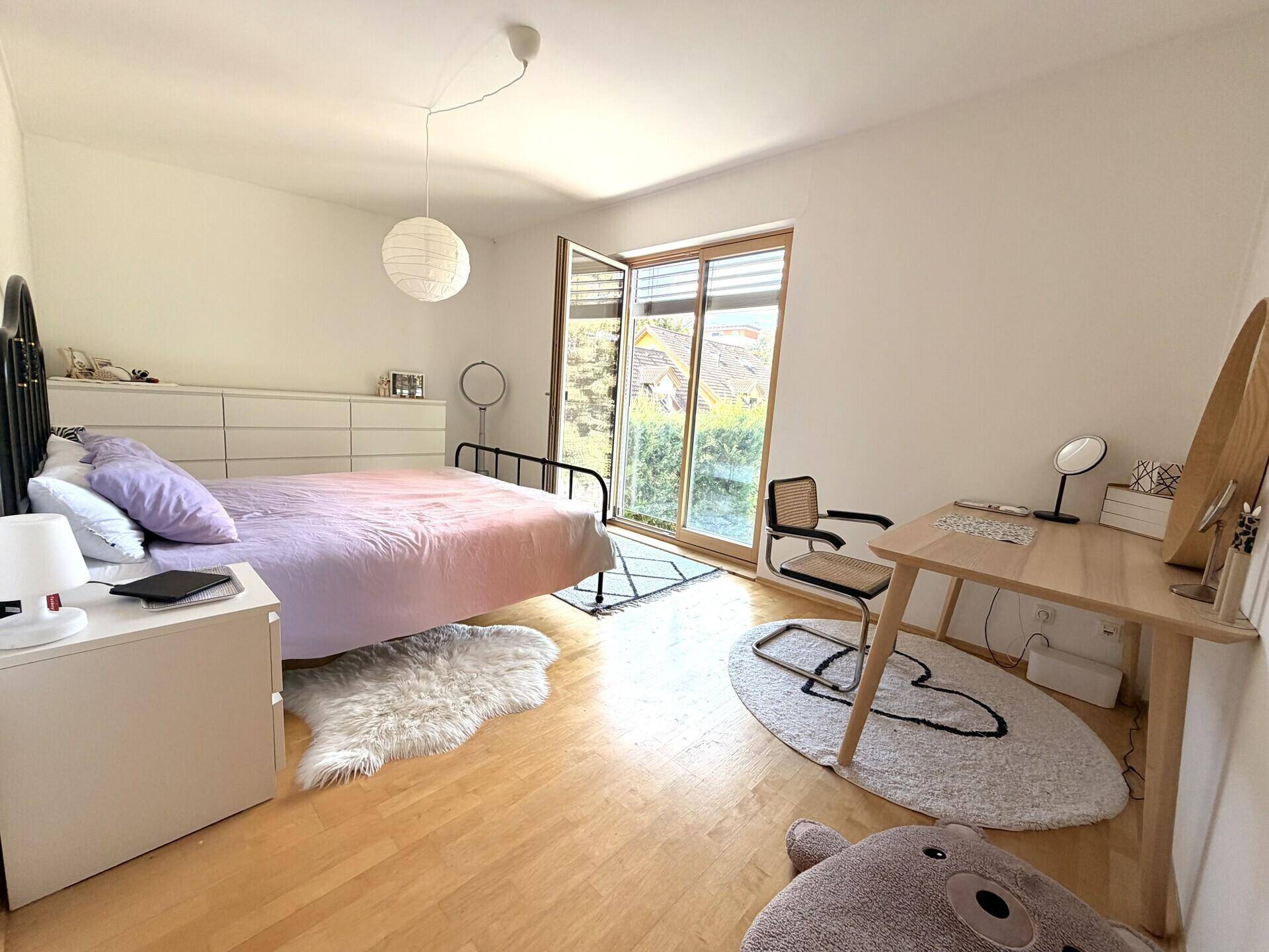 Schlafzimmer mit hellem Holzboden, Doppelbett und Zugang zu einem Balkon oder Terrasse.