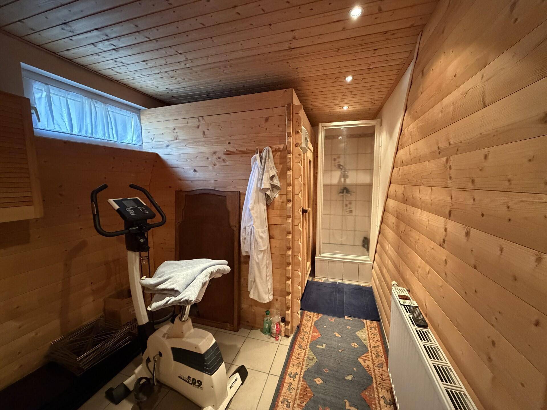 Gemütlicher Wellnessbereich mit Holzverkleidung, Sauna und Fitnessgerät für Entspannung und Sport.