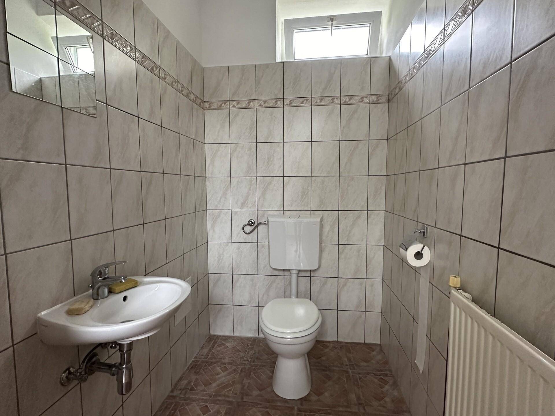 Kleines Gäste-WC mit Fenster, Toilette und Waschbecken, komplett gefliest in neutralen Farben.