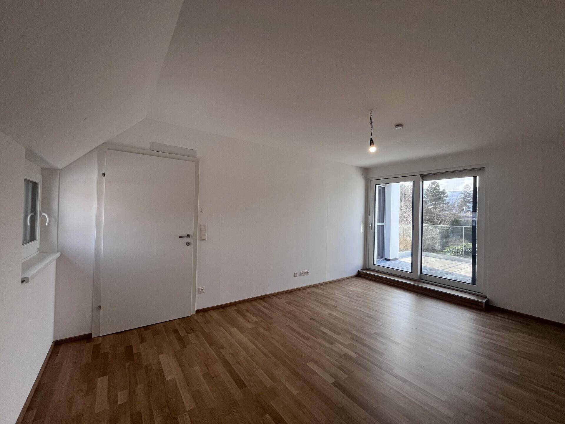 Schlafzimmer mit Parkettboden, weißer Tür und Fenster für natürliche Belichtung.