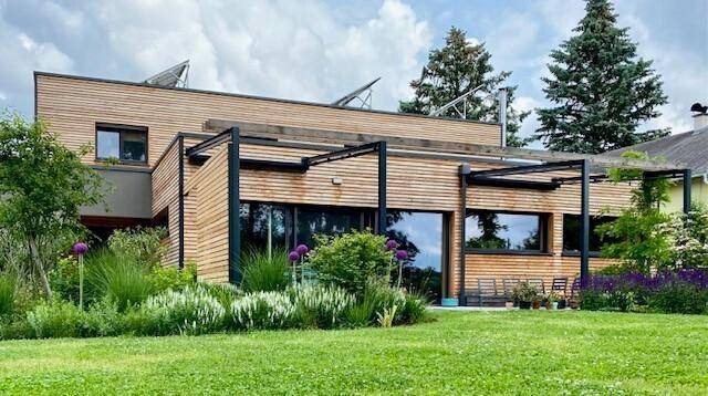 Modernes Haus mit Holzfassade, großem Garten und Photovoltaikanlage auf dem Dach.