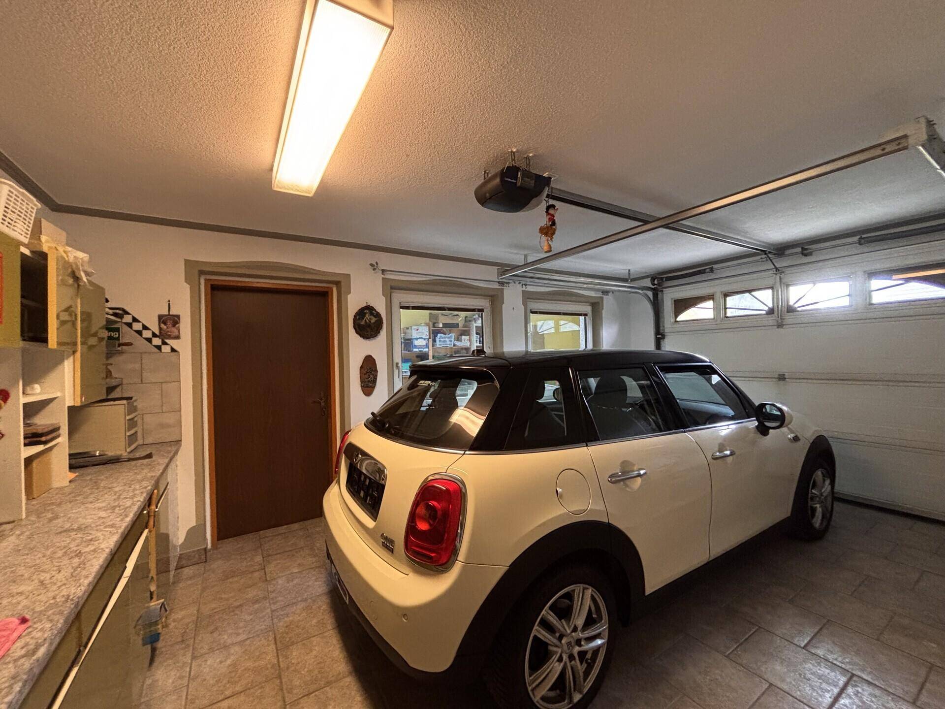 Geräumige Garage mit gefliestem Boden, einem geparkten Auto und Stauraum.