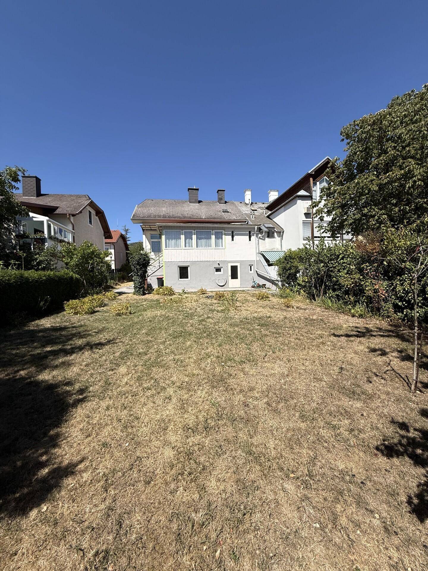Großer, sonniger Garten hinter dem Haus mit trockenem Rasen und Blick auf die umliegende Bebauung.