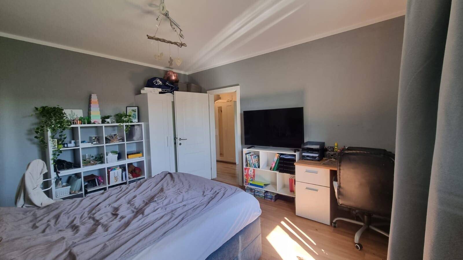 Geräumiges Schlafzimmer mit Bett, Regalen und einem Arbeitsbereich am Fenster.