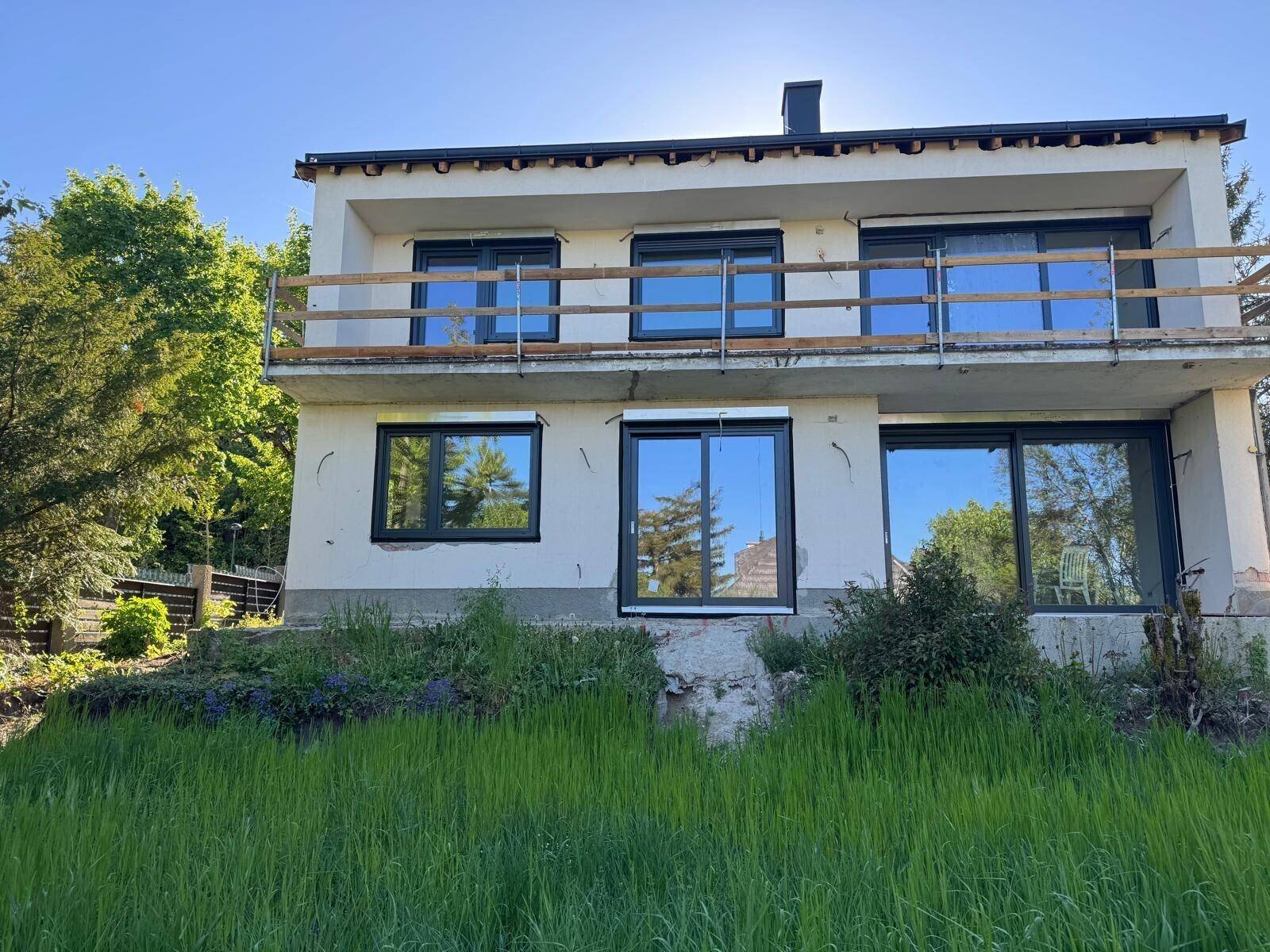 Fassade eines im Bau befindlichen Hauses mit neuen Fenstern und Balkon im Sonnenlicht.